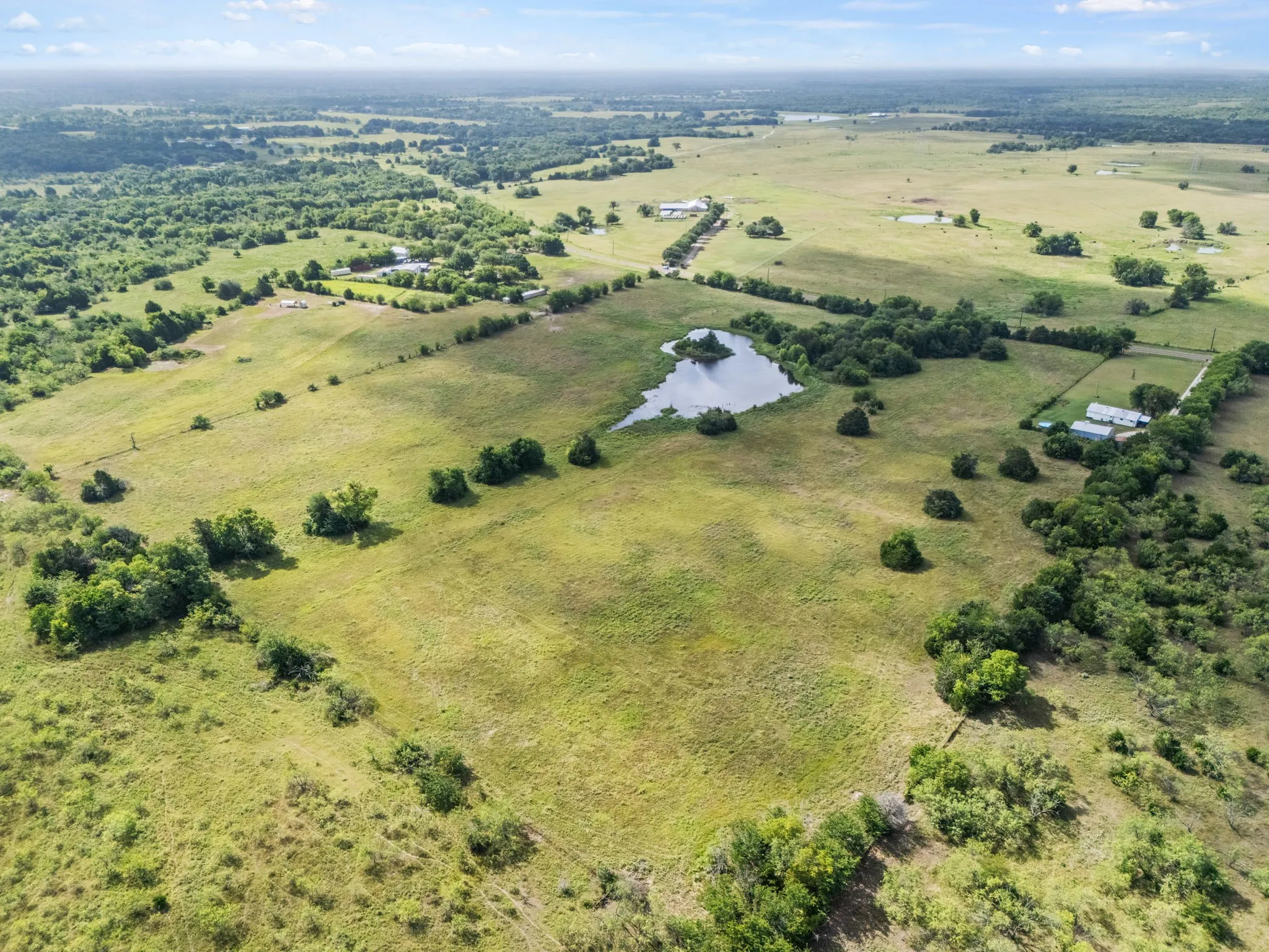 Expansive rural acreage featuring open fields, scattered trees, and a natural pond