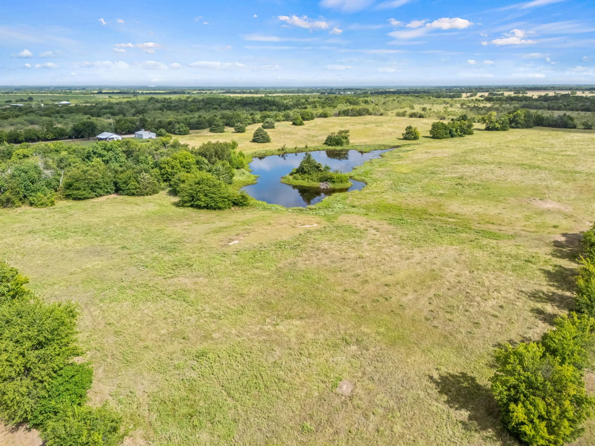 Expansive open land featuring a natural pond with a central island and scattered mature trees