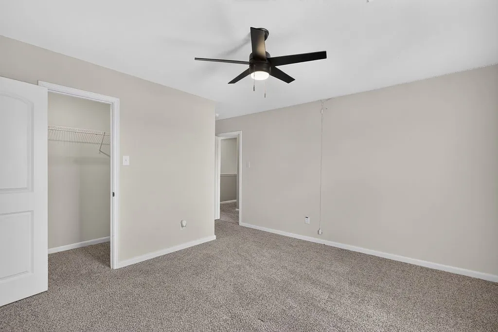 Carpeted room with light neutral walls, featuring a ceiling fan with integrated lighting, a closet with bifold doors and wire shelving, and white trim throughout