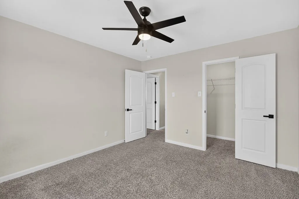 Room featuring neutral wall paint, gray carpeting, a dark-toned ceiling fan with lighting, white interior doors with dark hardware, and a wire rack closet system
