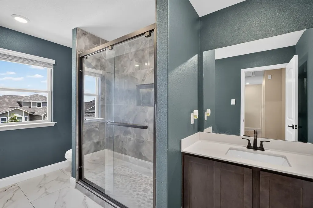 Bathroom featuring a spacious walk-in shower with glass enclosure and pebble flooring, complemented by large-format marble-look floor tiling