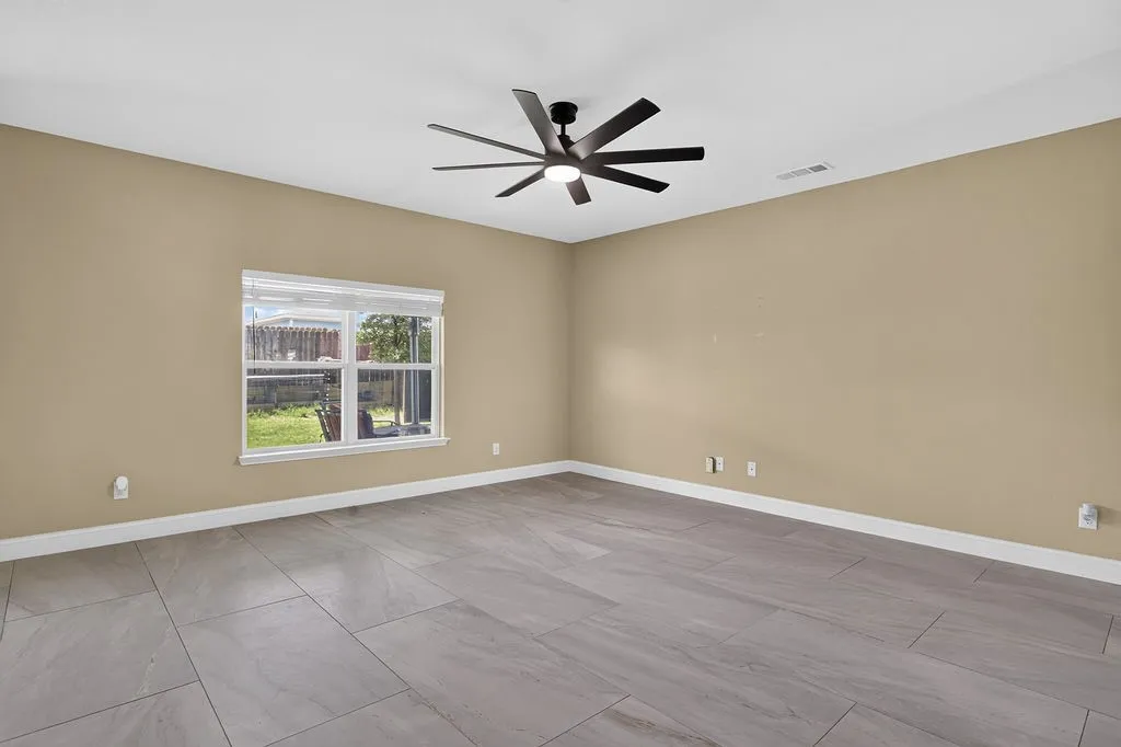 Spacious room featuring neutral tone walls, large format tile flooring, white baseboards, and a modern multi-blade ceiling fan