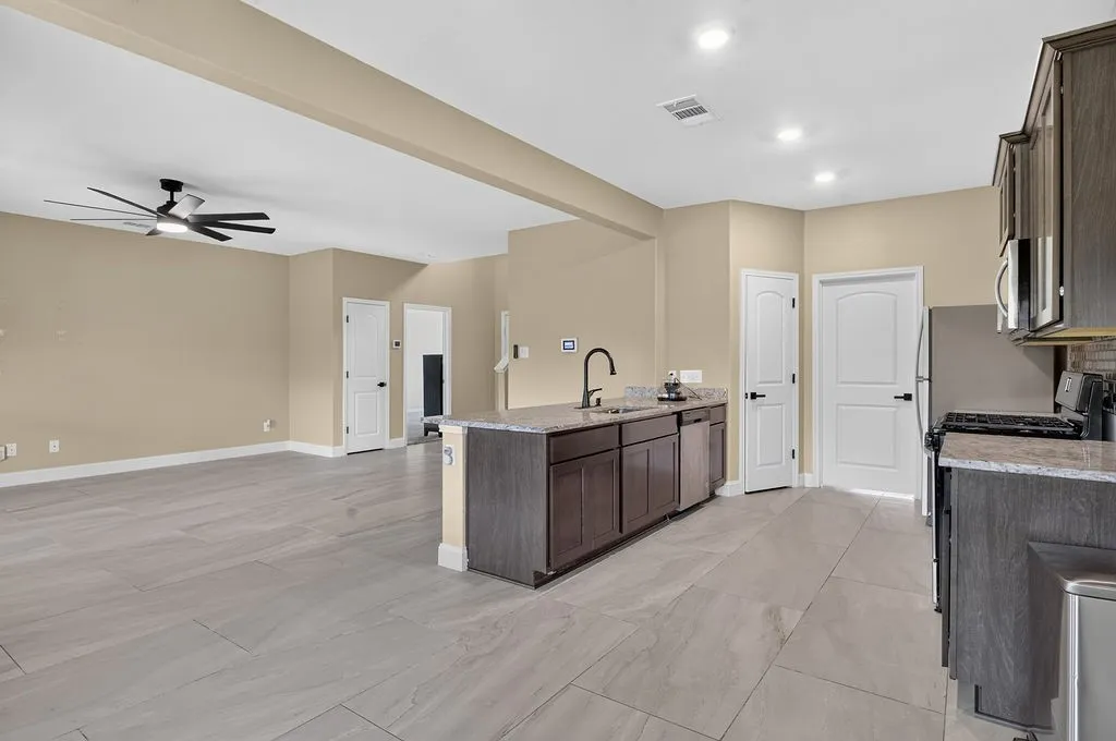 Spacious open-concept living area featuring light-toned flooring, a modern ceiling fan, recessed lighting, and a kitchen island with stone countertops and a gooseneck faucet