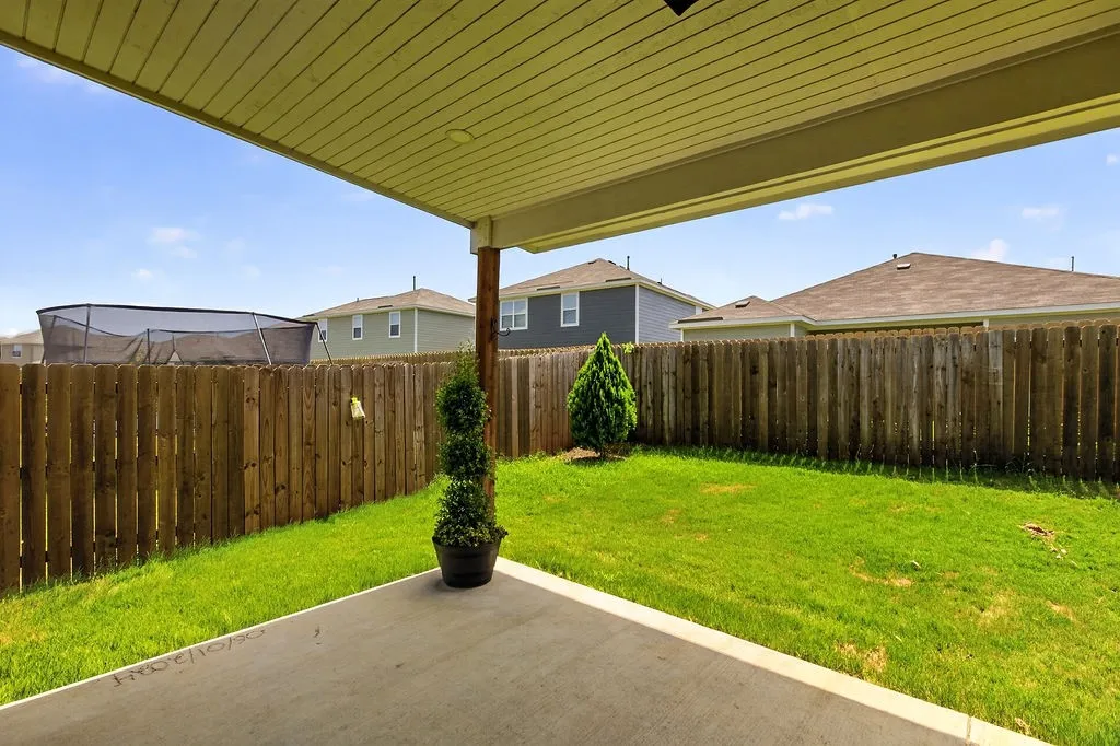 Expansive backyard featuring a concrete patio, a manicured lawn, a full privacy fence, and a covered patio area with a light-colored soffit