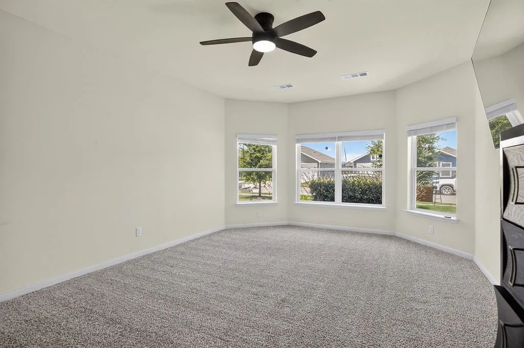 Carpeted interior space featuring a multi-windowed bay wall, a ceiling fan with integrated lighting, and neutral wall tones