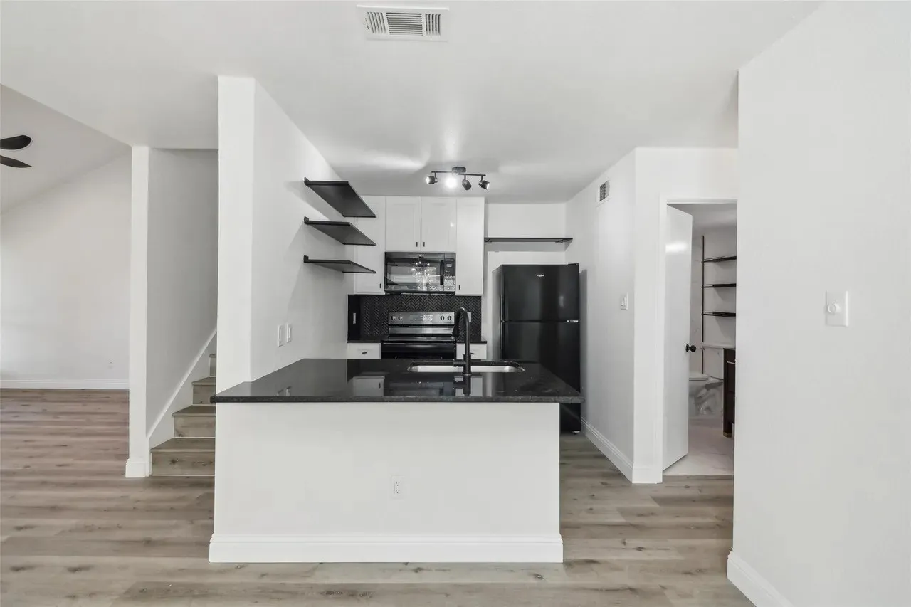 Modern kitchen featuring an island with a black countertop, black appliances, white cabinetry, and open shelving