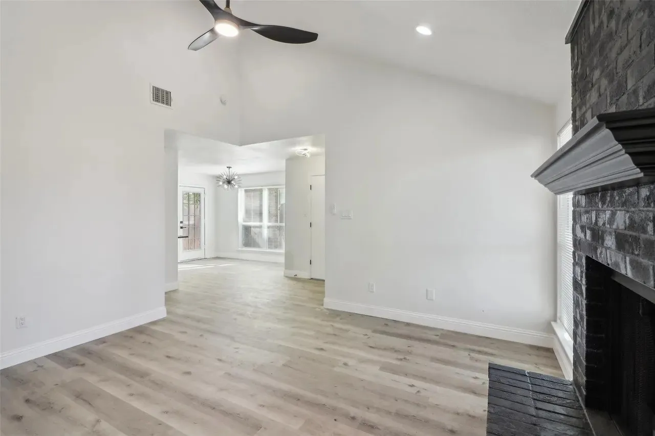 Spacious room featuring vaulted ceilings, wood-finish flooring, a contemporary ceiling fan, and a black brick fireplace with a decorative mantel