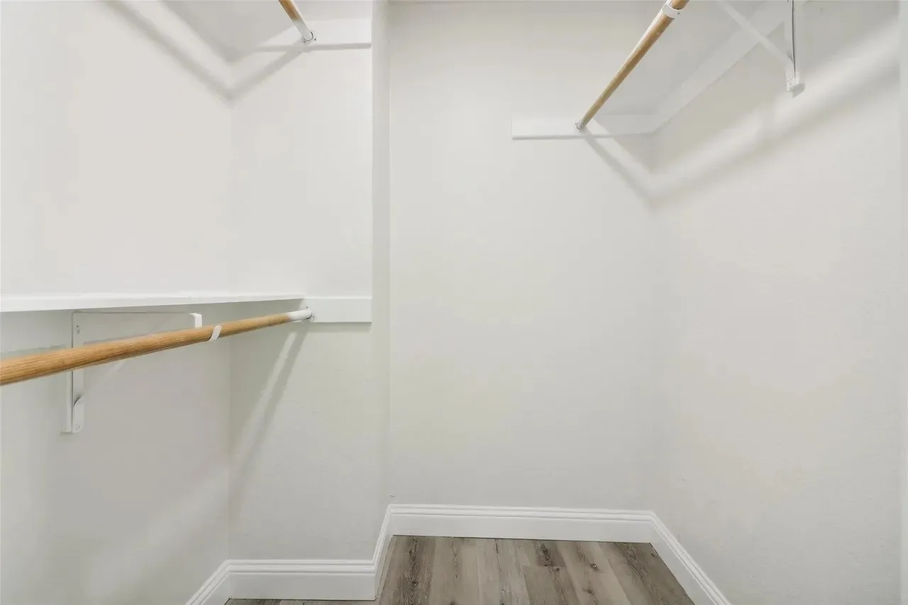 Walk-in closet with multiple hanging rods, integrated shelving, white walls, and wood-finish flooring
