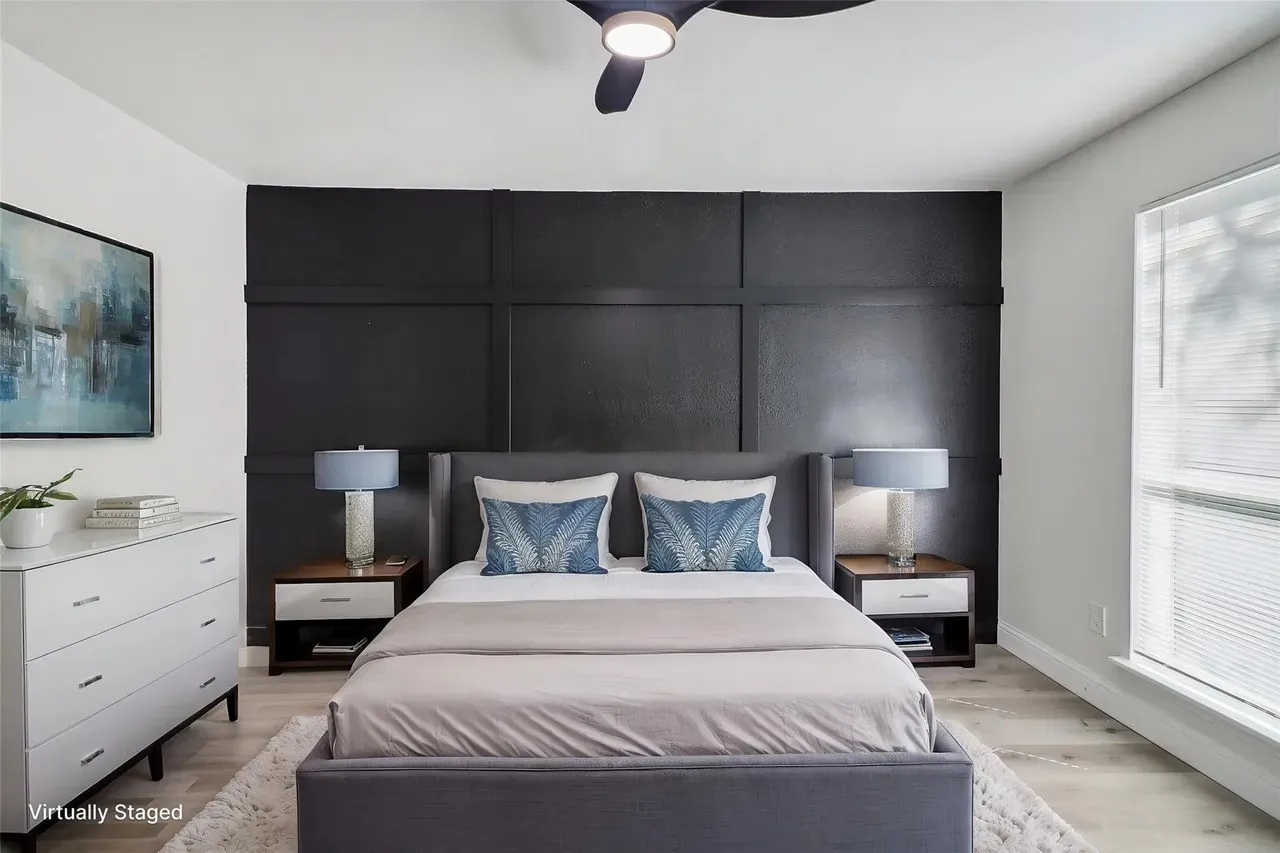 Bedroom featuring a striking dark accent wall with paneling, a ceiling fan, and wood-finish flooring