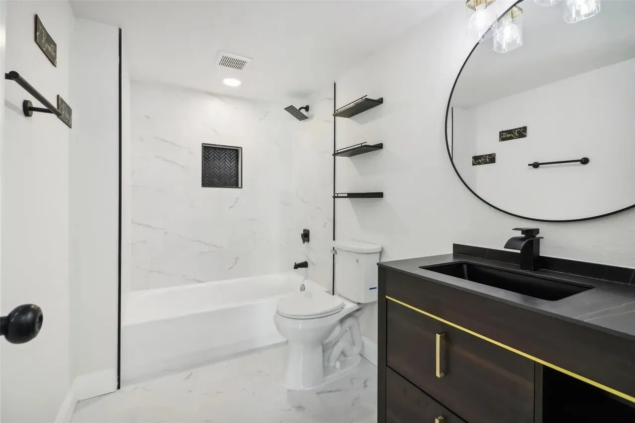 Bathroom featuring a dark wood-finish vanity with gold-tone hardware, a circular mirror, and a white tiled shower with a black herringbone accent niche