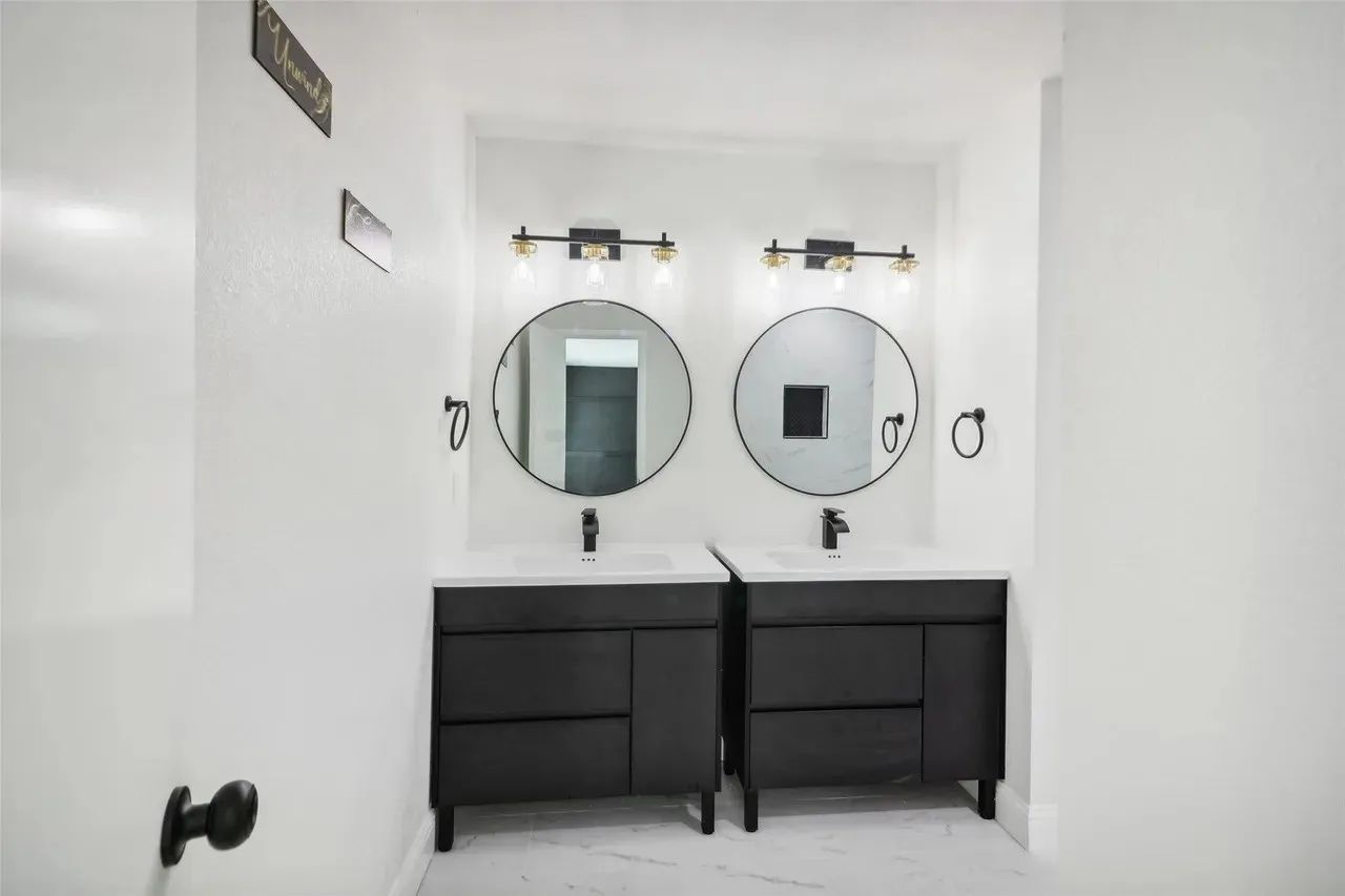Dual vanity setup featuring black cabinetry, white countertops, and circular mirrors with black frames