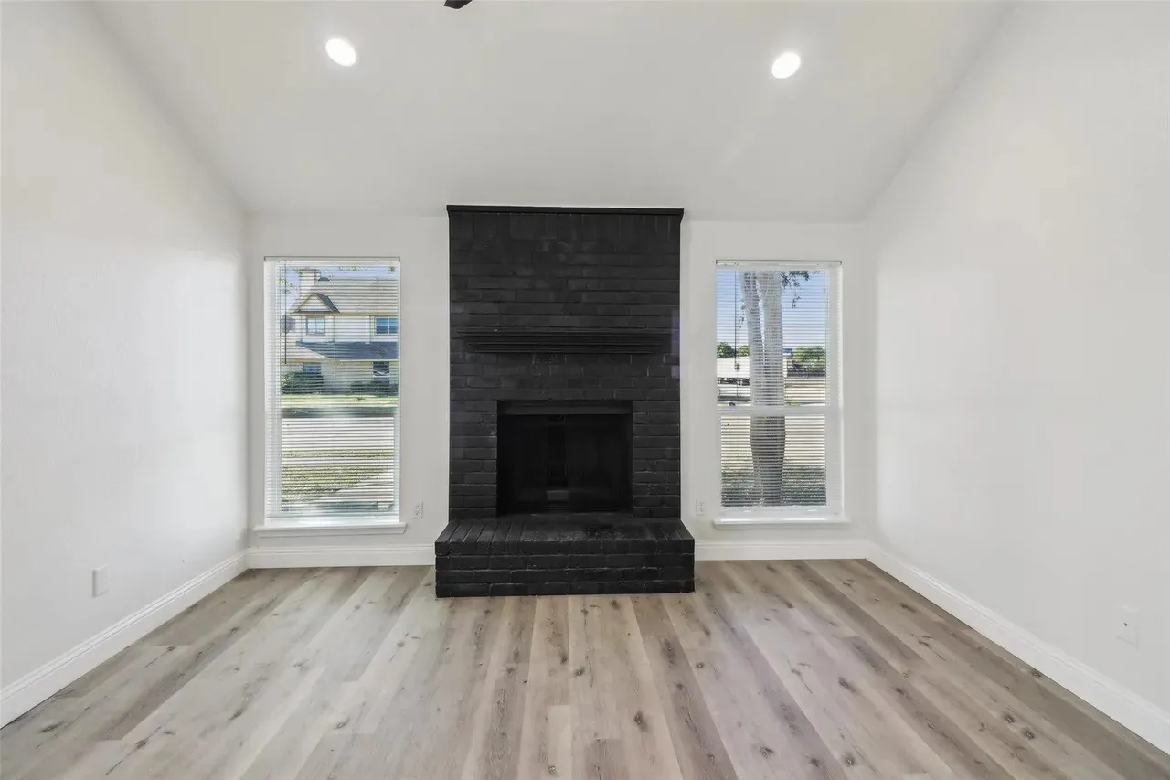 Living space featuring a prominent black brick fireplace, vaulted ceiling with recessed lighting, and wood-finish flooring