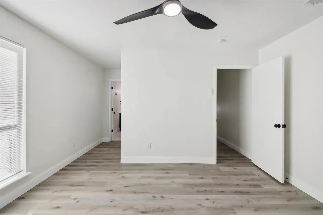 Spacious room featuring light wood-finish flooring, white walls, and a modern ceiling fan with integrated lighting