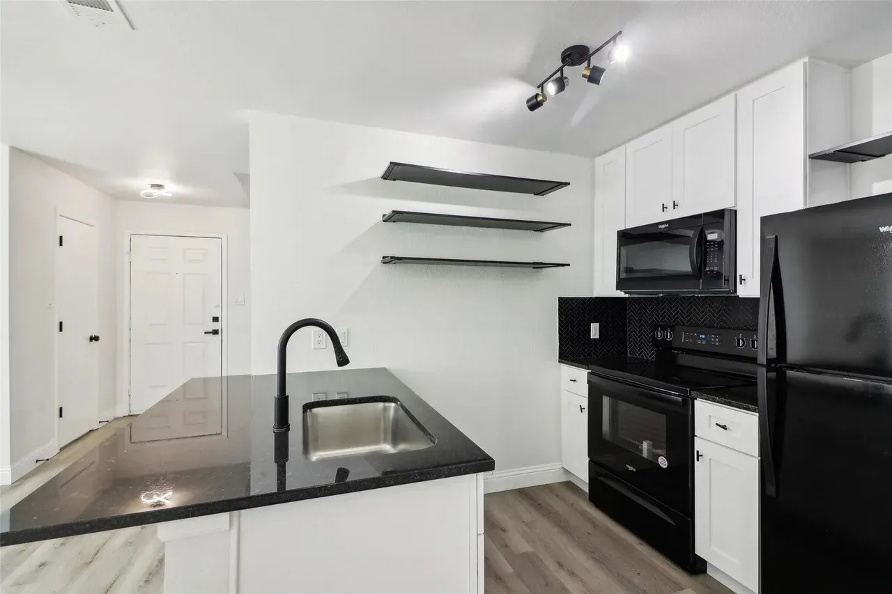 Modern kitchen featuring white cabinetry, black granite countertops, stainless steel sink with matte black faucet, and chevron pattern backsplash