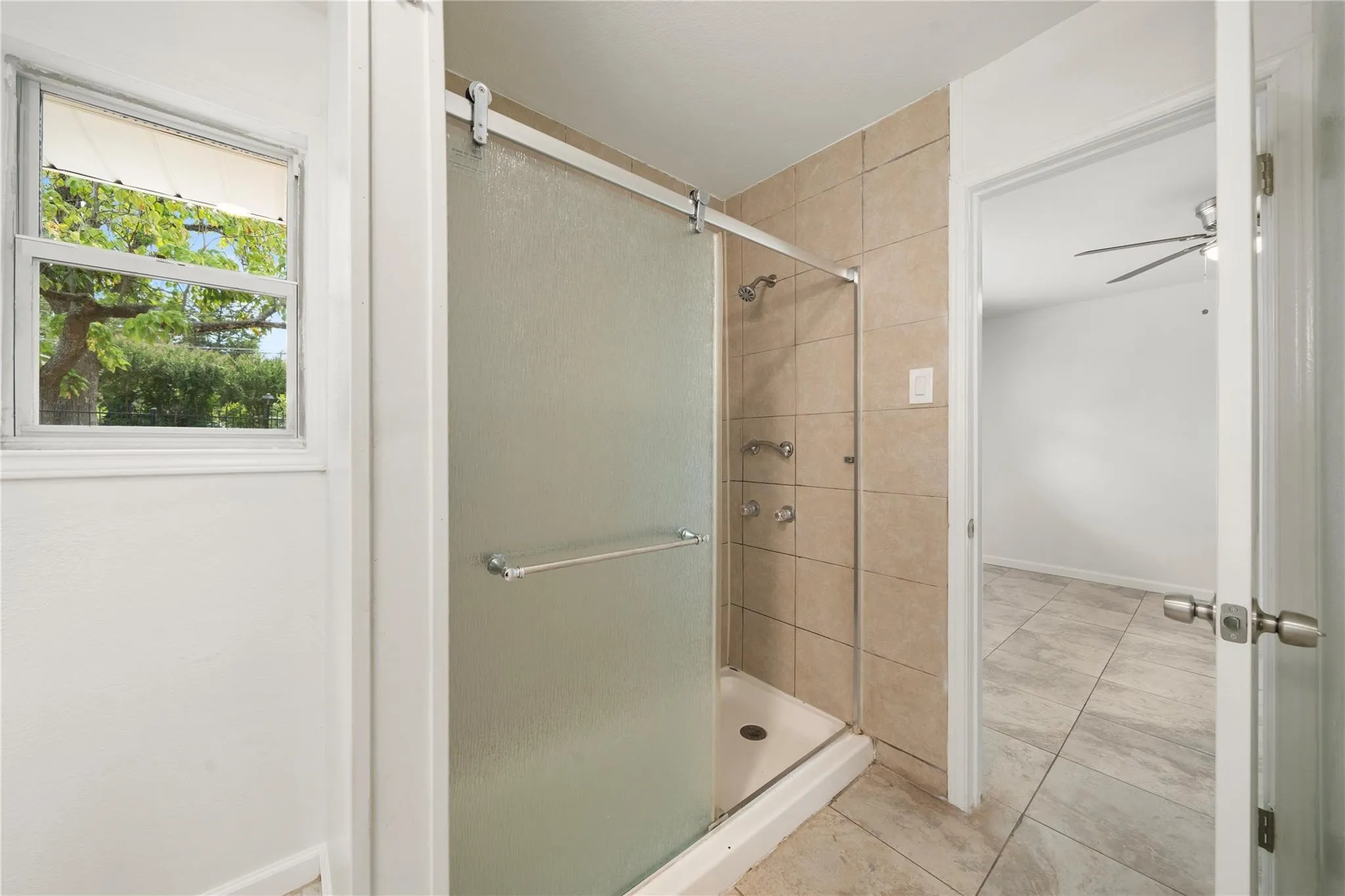 Tiled shower with frosted glass enclosure, wall-mounted showerhead, and grab bars