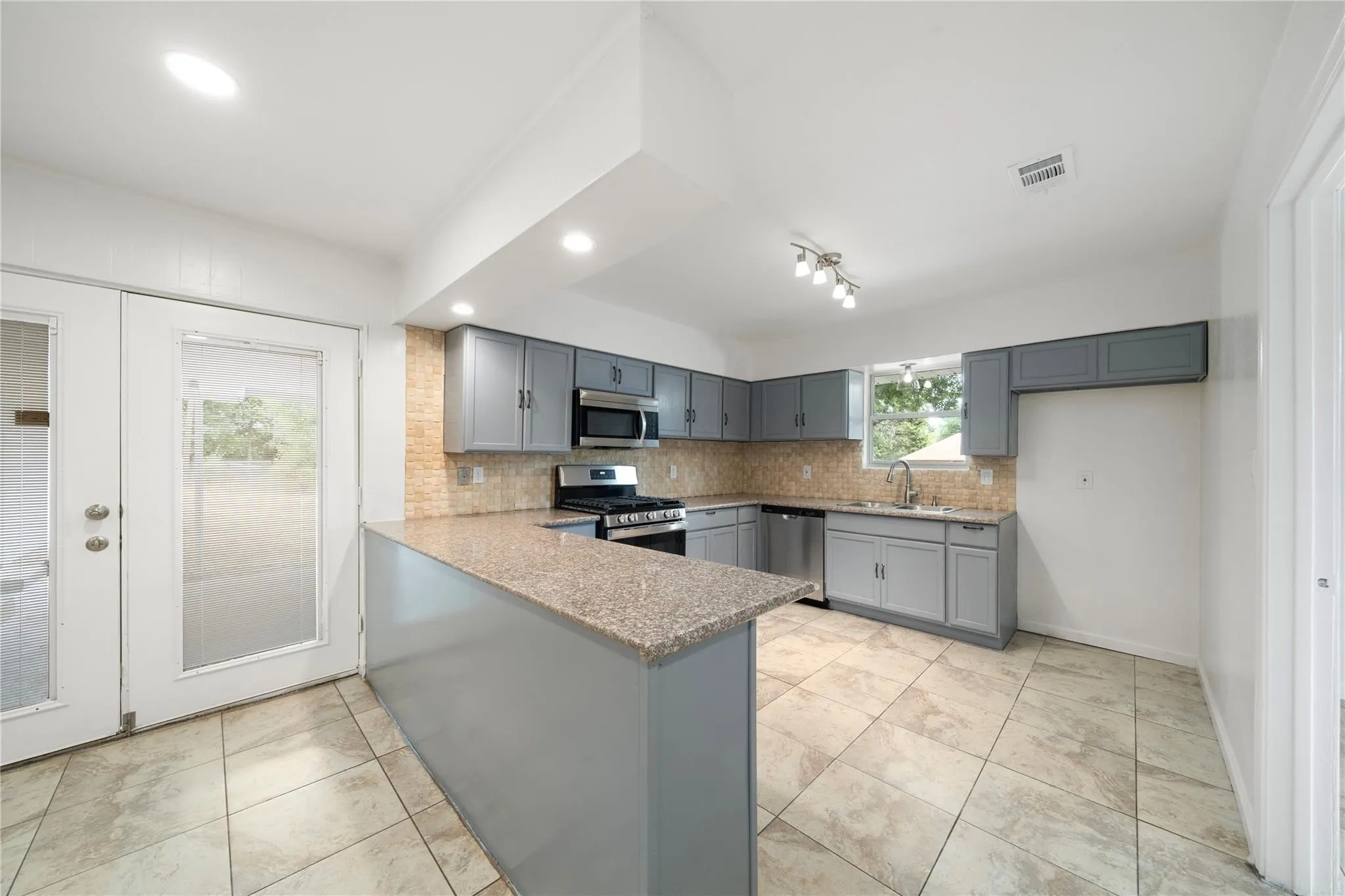 Kitchen featuring gray cabinetry, stone-look countertops, stainless steel appliances, and a tiled backsplash