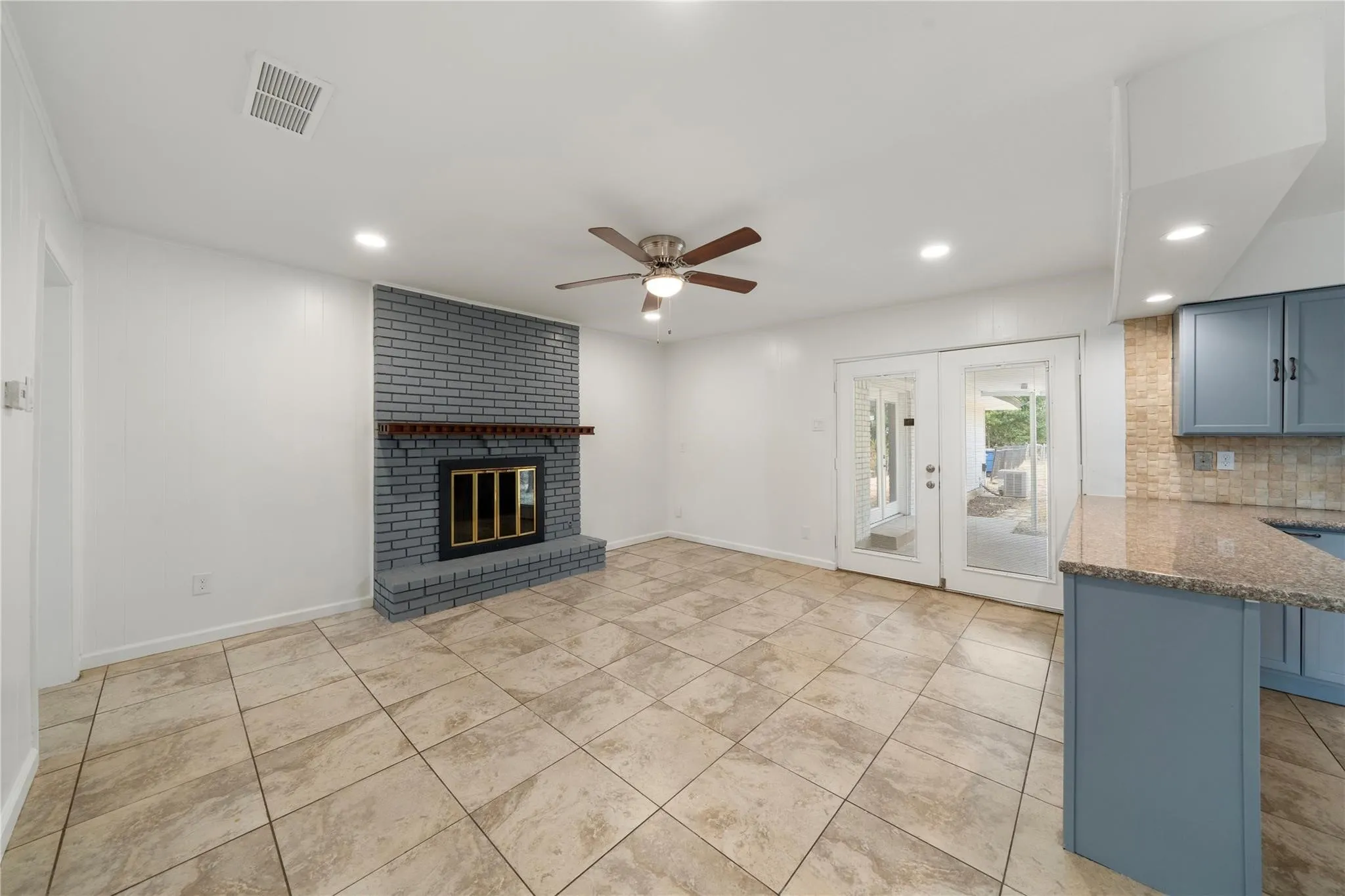Living area with tile flooring and a gray brick fireplace featuring a wood mantel