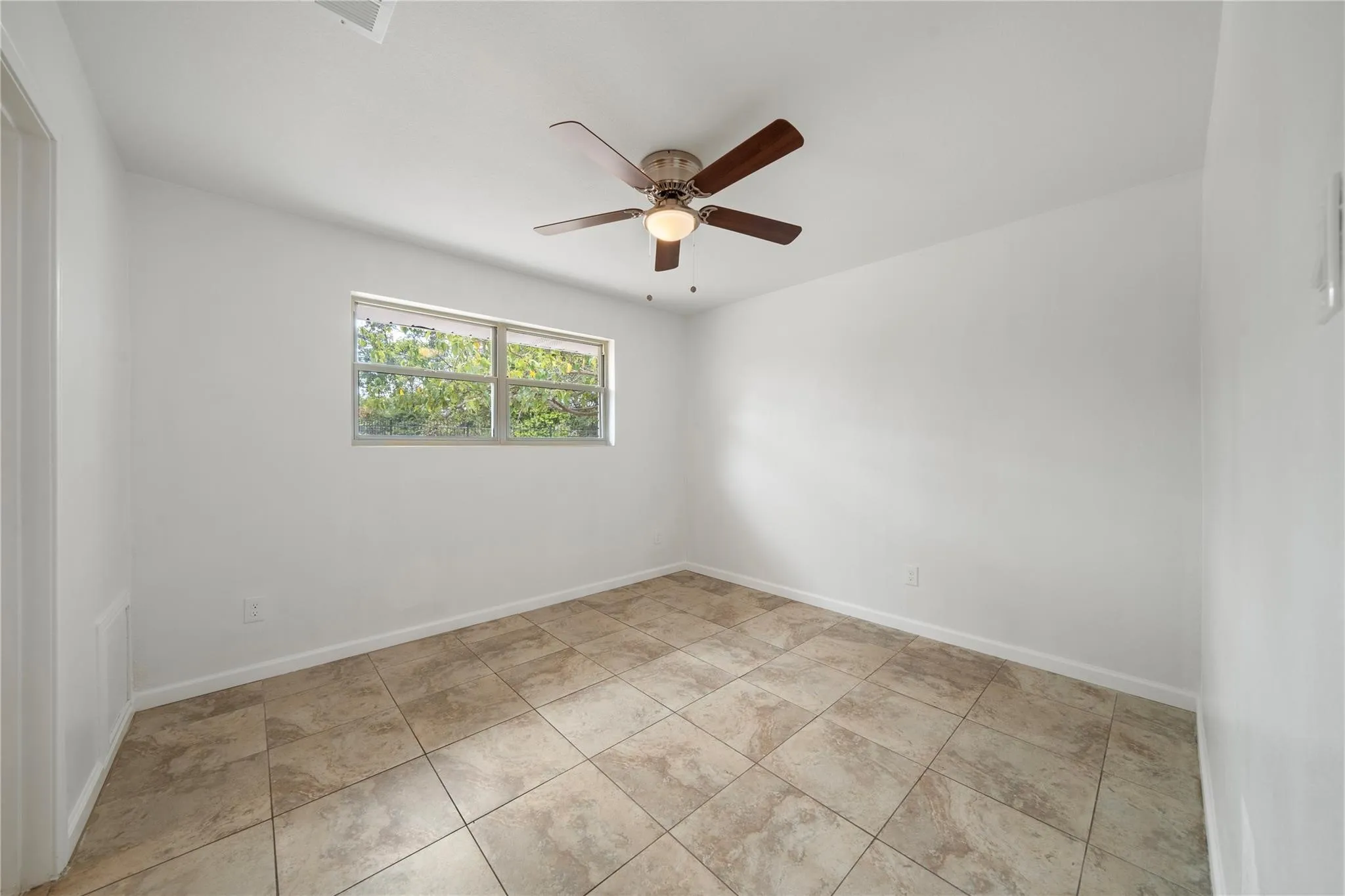 Room featuring neutral-toned tile flooring, white walls, and a ceiling fan with light fixture