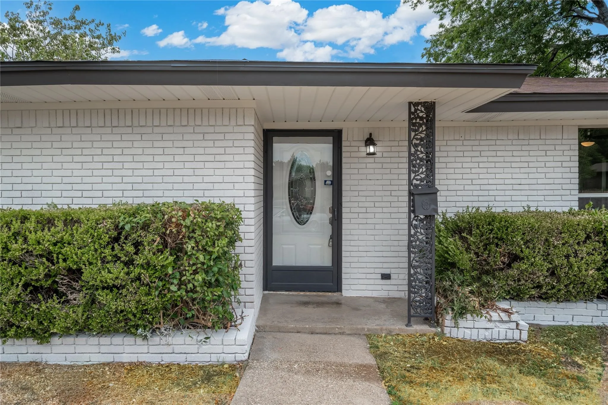 White brick exterior with dark trim and a decorative metal support column