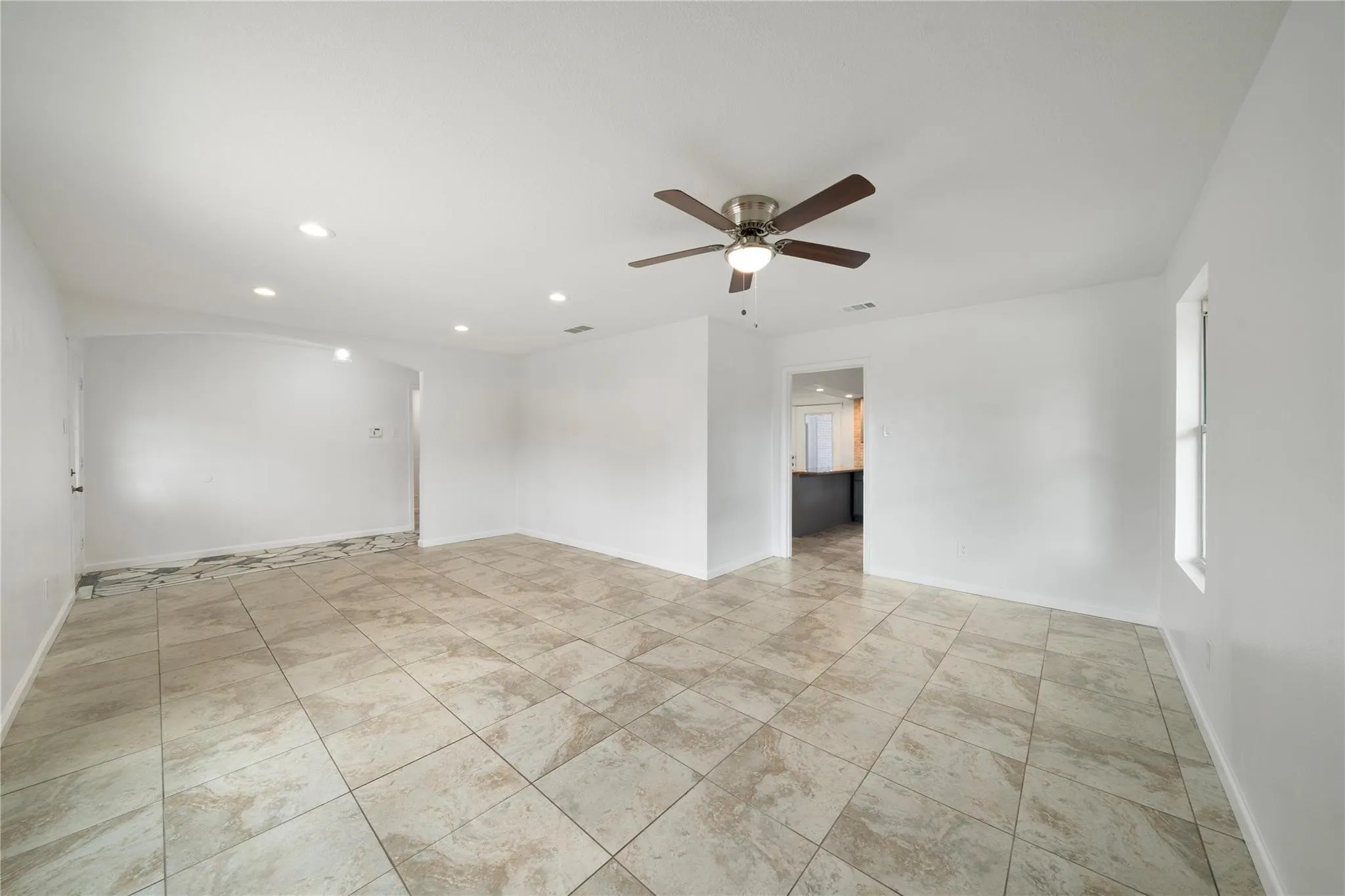 Spacious room featuring large format tile flooring, recessed ceiling lighting, a ceiling fan with integrated light, and white painted walls