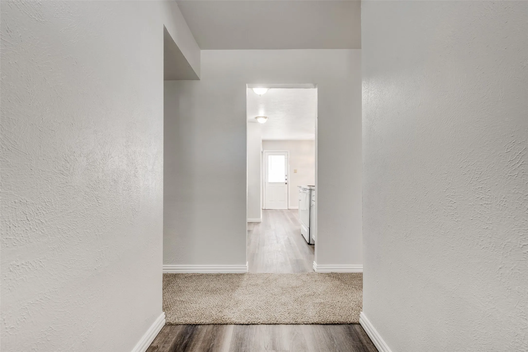Hallway with textured neutral walls, wood-finish flooring, and light carpeting