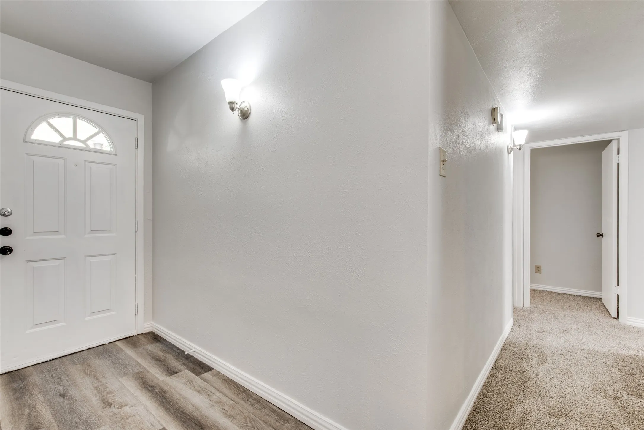 Entryway featuring wood-finish flooring transitioning to carpeted hallway