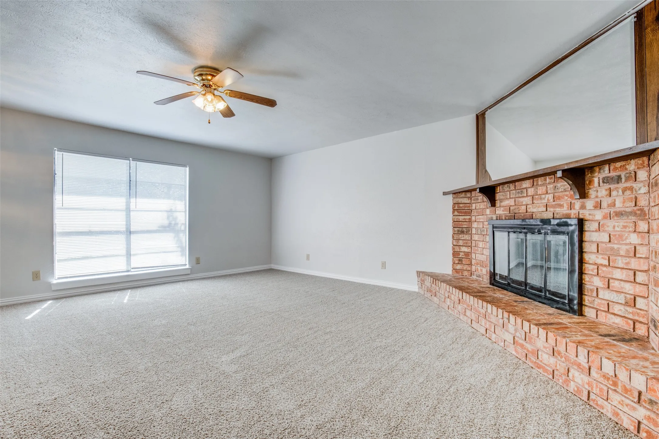 Spacious interior featuring a brick fireplace with a raised hearth, a wood mantel, and an integrated mirror