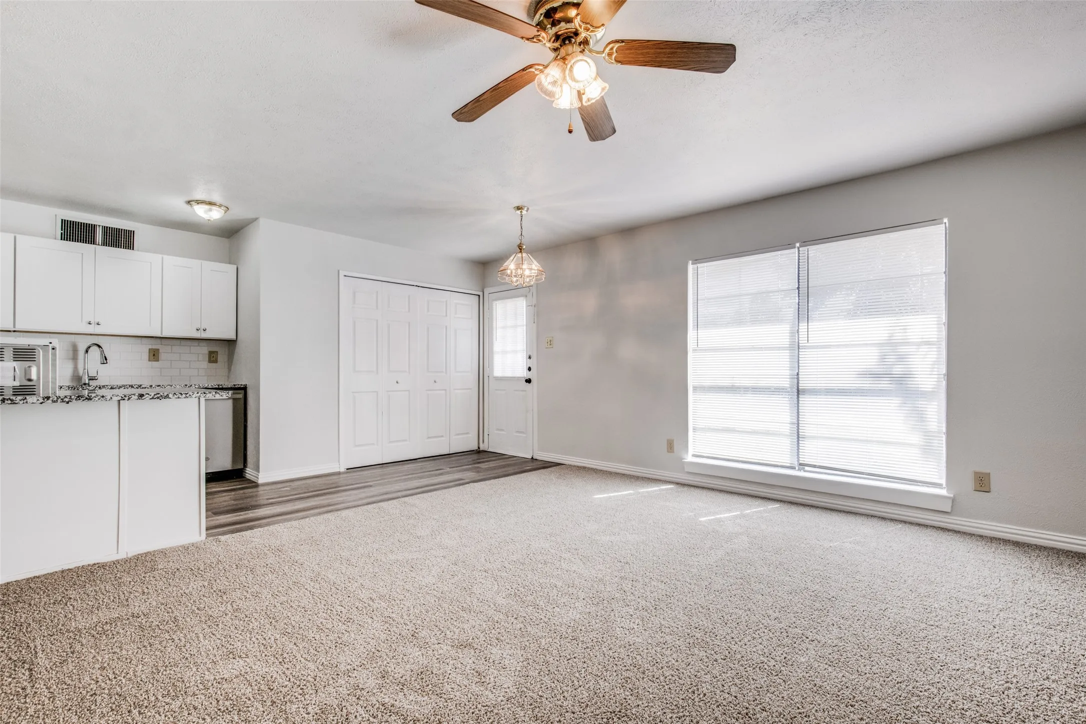 Open-concept living area featuring a ceiling fan, wall-to-wall carpeting, and wood-finish flooring