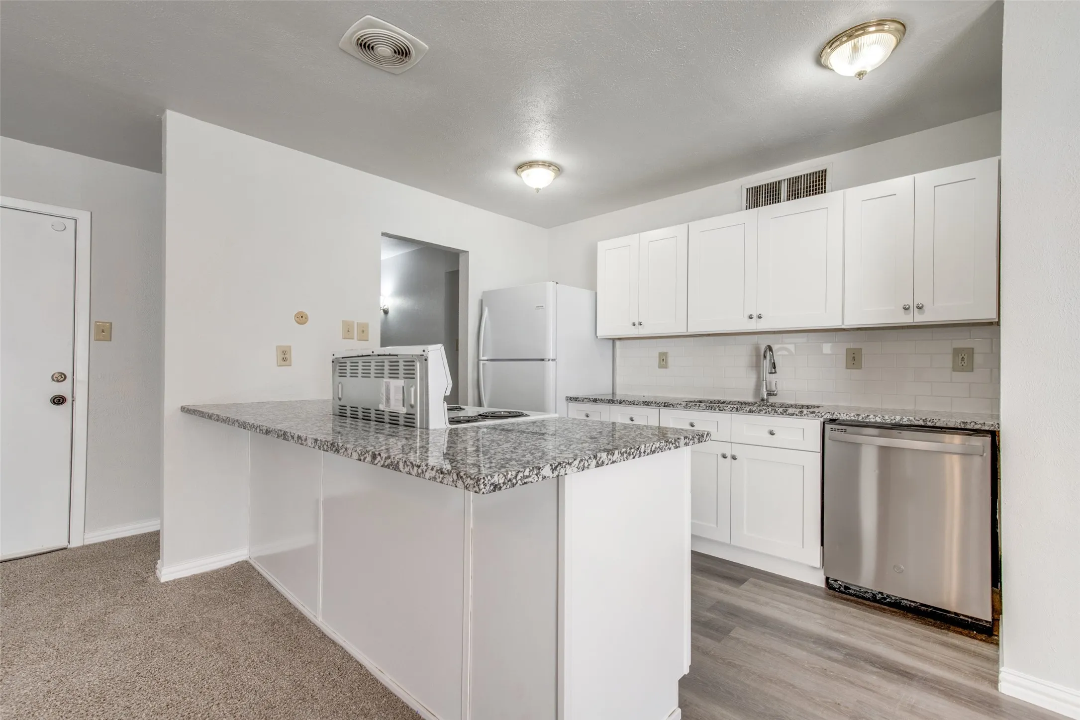 Kitchen featuring white shaker cabinetry, speckled countertops, a subway tile backsplash, stainless steel dishwasher, and wood-finish flooring