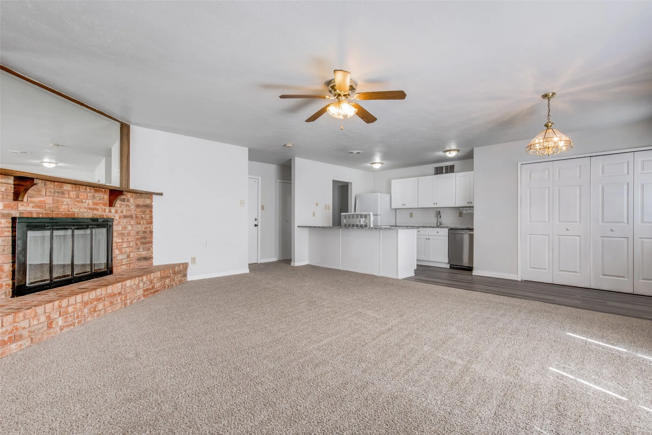 Open-concept living area featuring a brick fireplace, ceiling fan, and light-toned carpeting