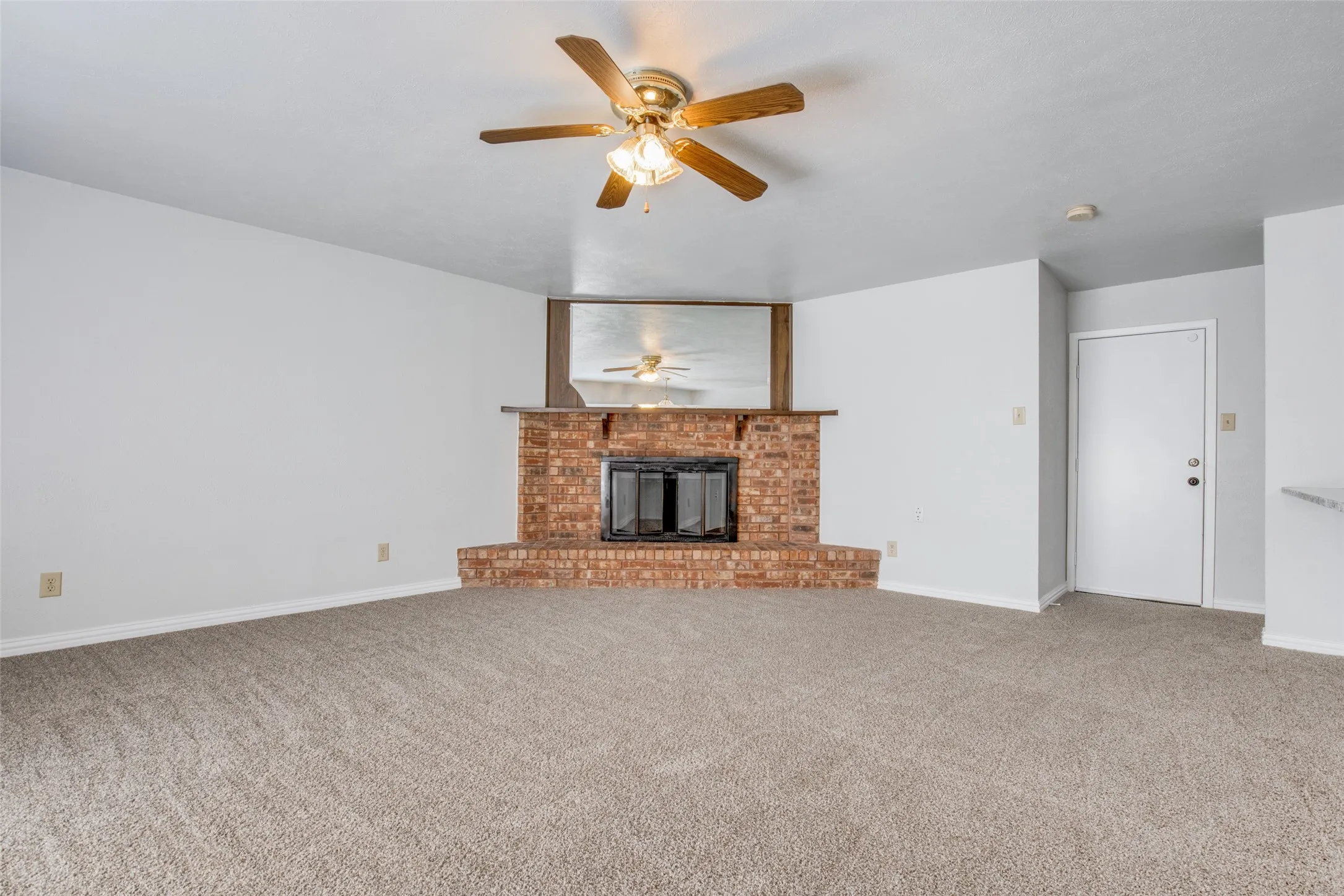Brick fireplace with a black firebox and a wood-finish mantel, illuminated by a ceiling fan with integrated lighting