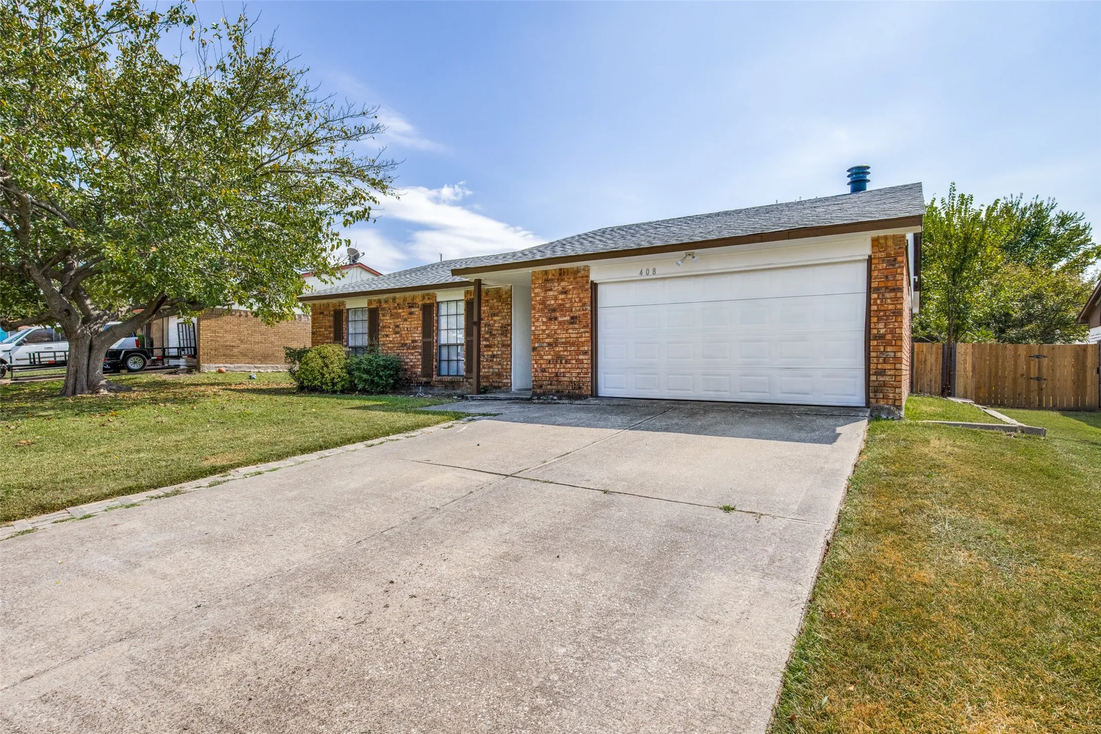 Front exterior featuring a brick facade, white garage door, and mature tree