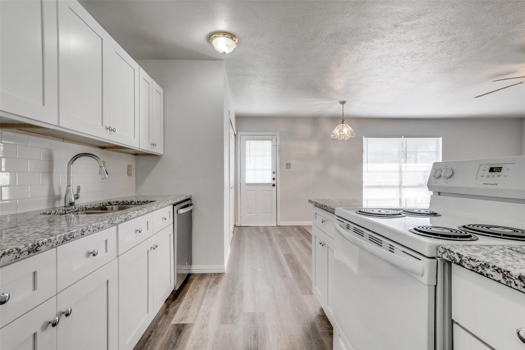 Kitchen featuring white cabinetry with silver hardware, speckled countertops, stainless steel sink with gooseneck faucet, subway tile backsplash, and wood-finish flooring