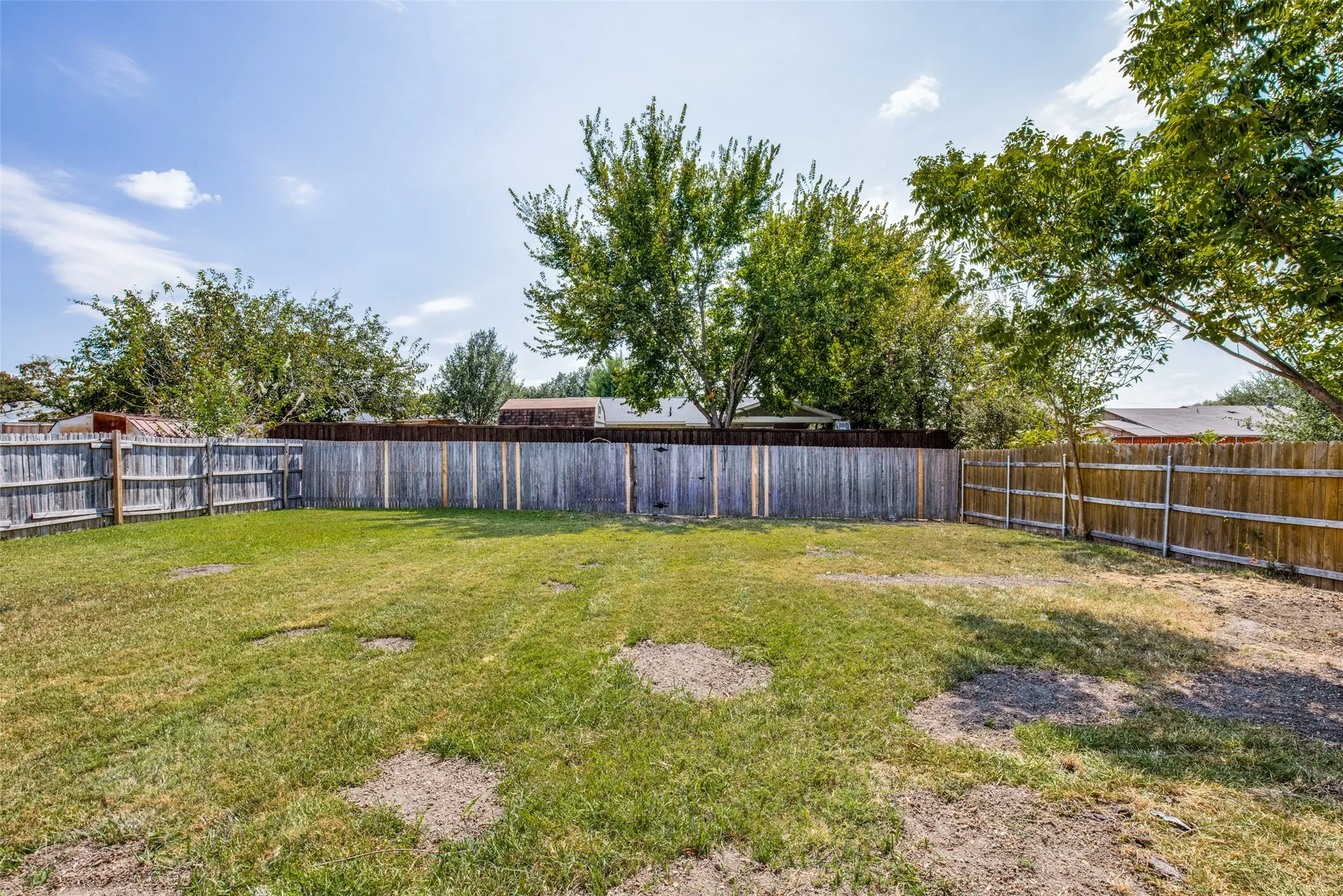 Spacious backyard featuring a full perimeter wooden privacy fence and mature trees