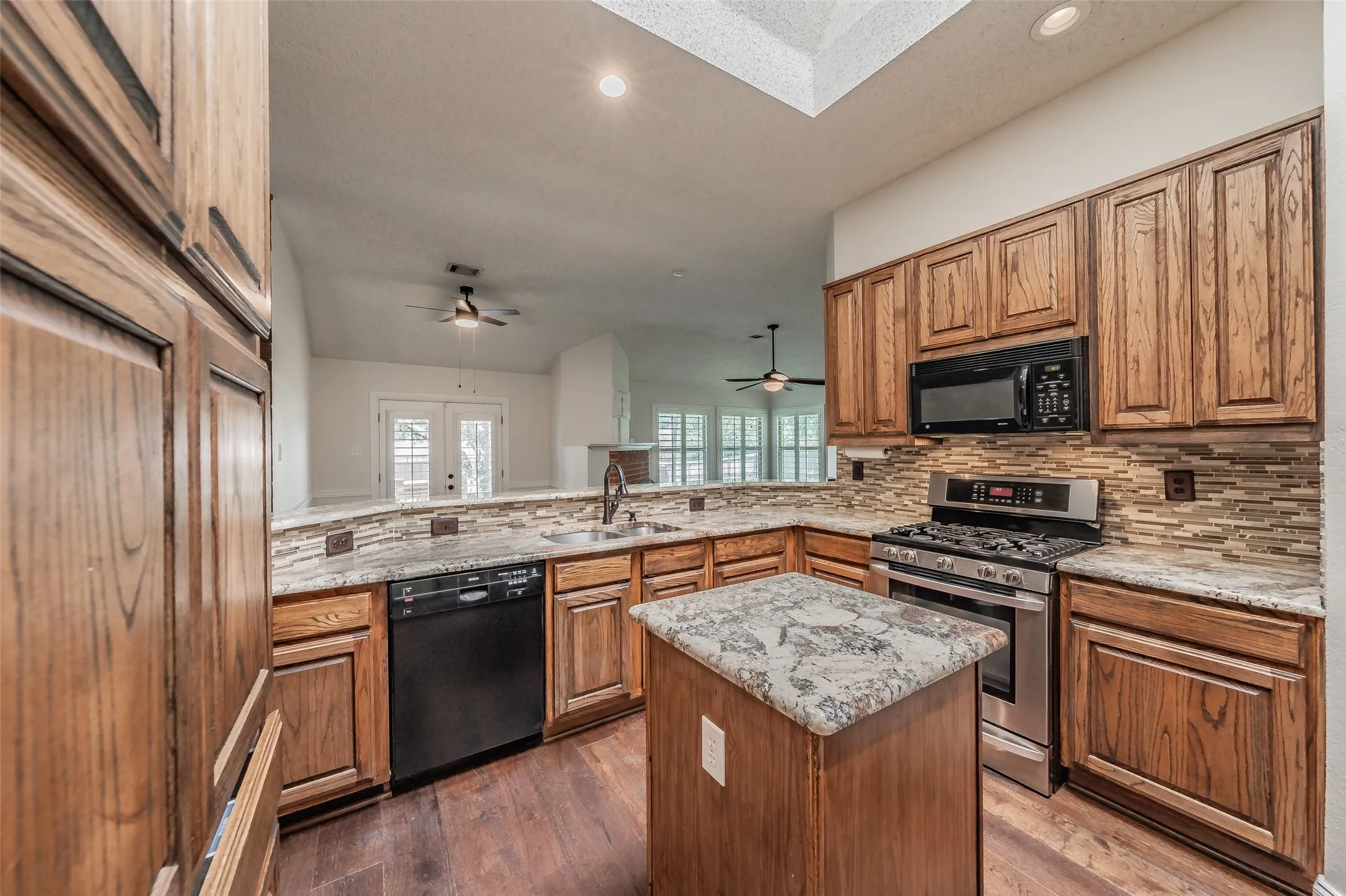 Kitchen featuring wood-finish cabinetry, granite countertops, tile backsplash, and stainless steel appliances