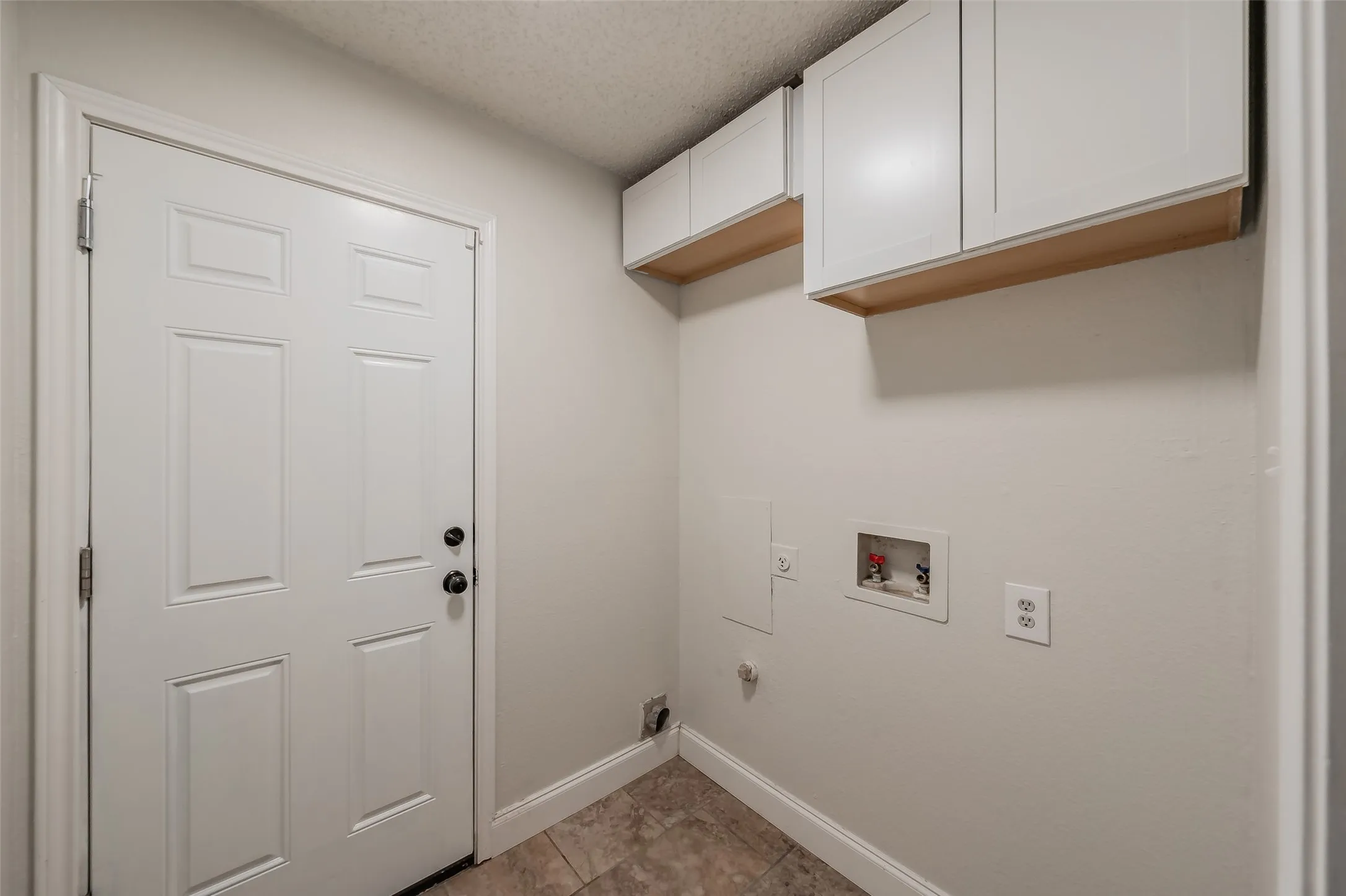 Utility area as you go into garage features ceramic tile and storage cabinets.