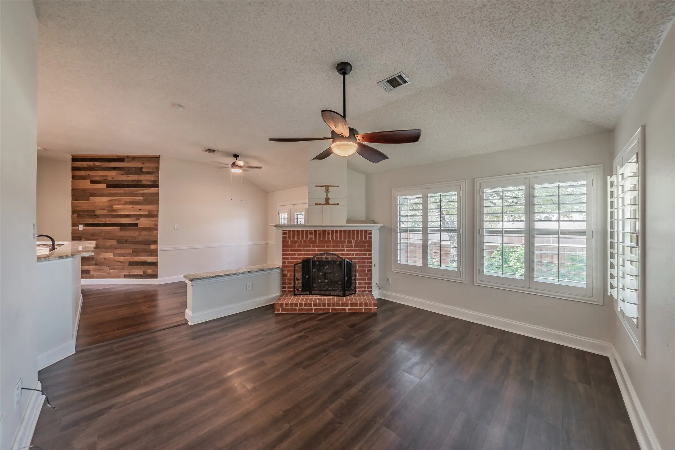 Living area featuring wood-finish flooring, a brick fireplace, vaulted ceilings, and windows with plantation shutters