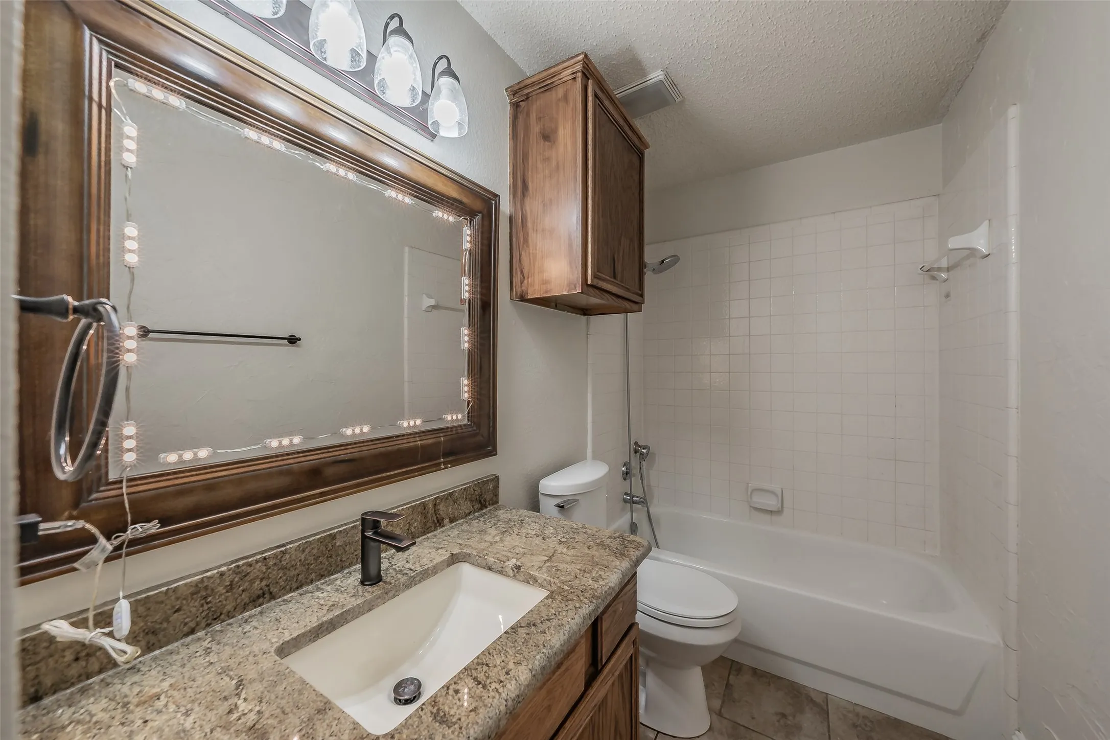 Bathroom featuring a vanity with a granite counter, framed mirror with additional lighting and upper cabinet for added storage.