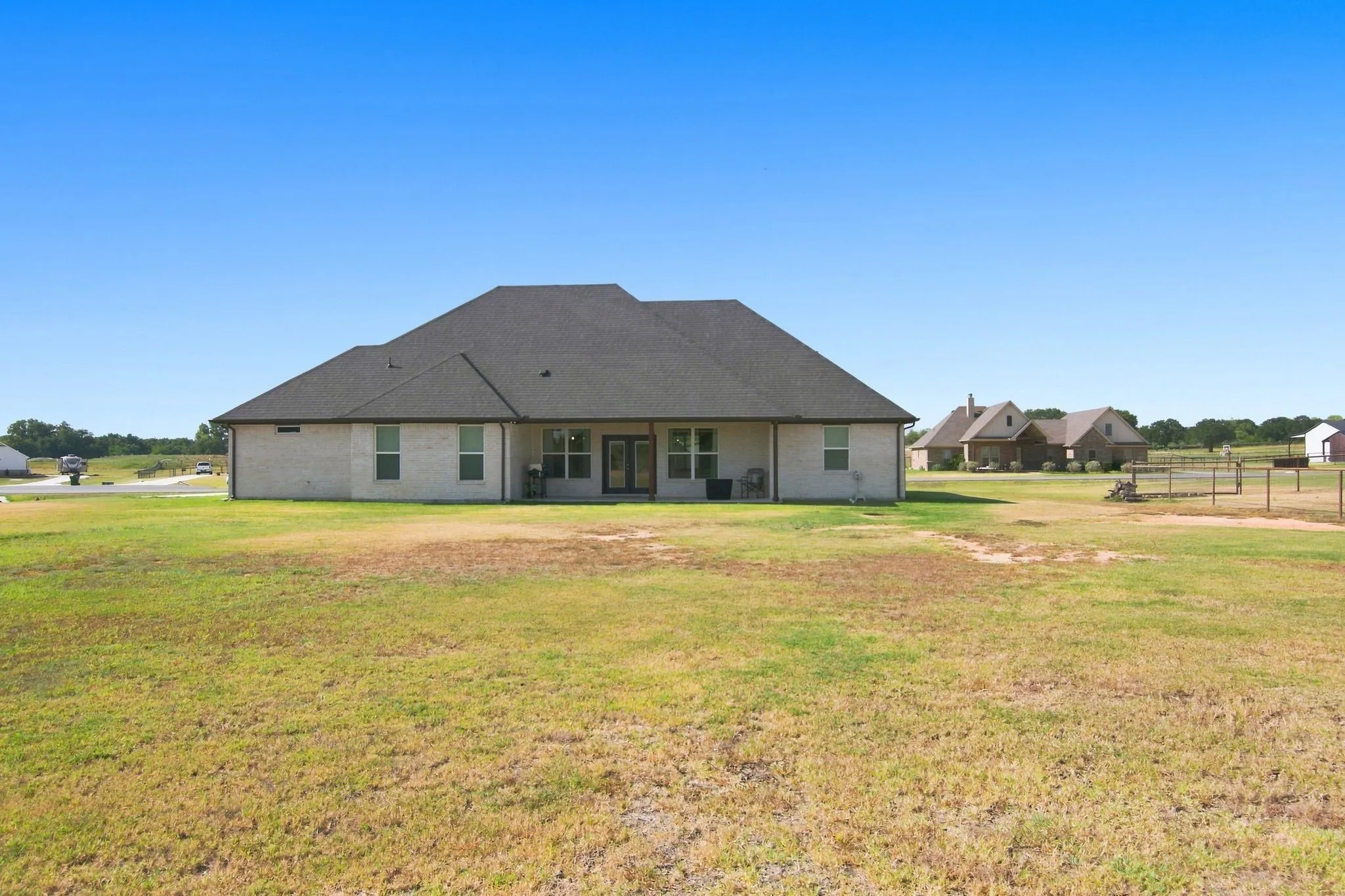Expansive backyard featuring a light brick exterior, dark gabled roof, covered patio, and dual glass-paned doors