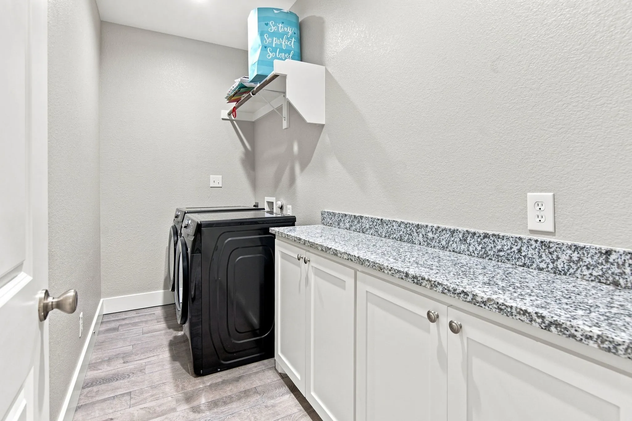 Laundry area featuring wood-finish flooring, white cabinetry, and a speckled countertop
