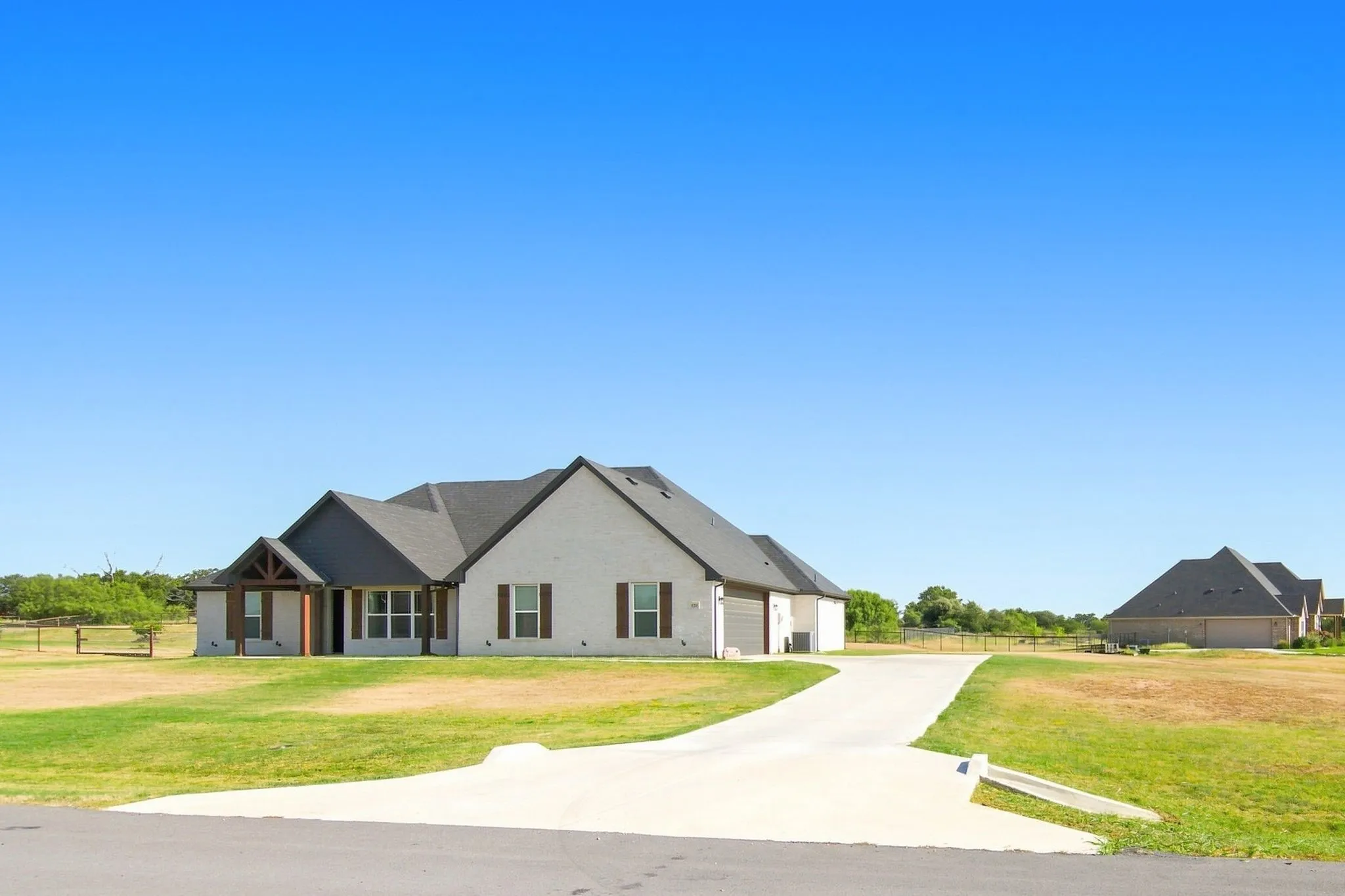 Expansive property featuring a light-colored brick exterior, dark shingle roof, and a prominent concrete driveway
