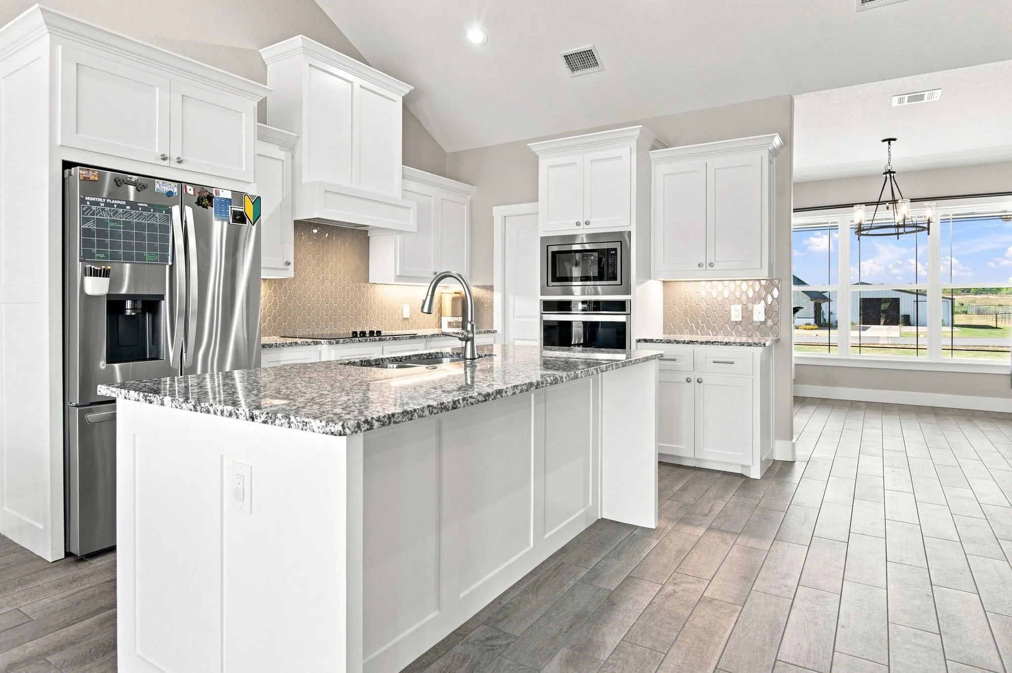 Spacious kitchen featuring an island with a light-toned countertop, white cabinetry, stainless steel appliances, a tile backsplash, and light wood-finish flooring