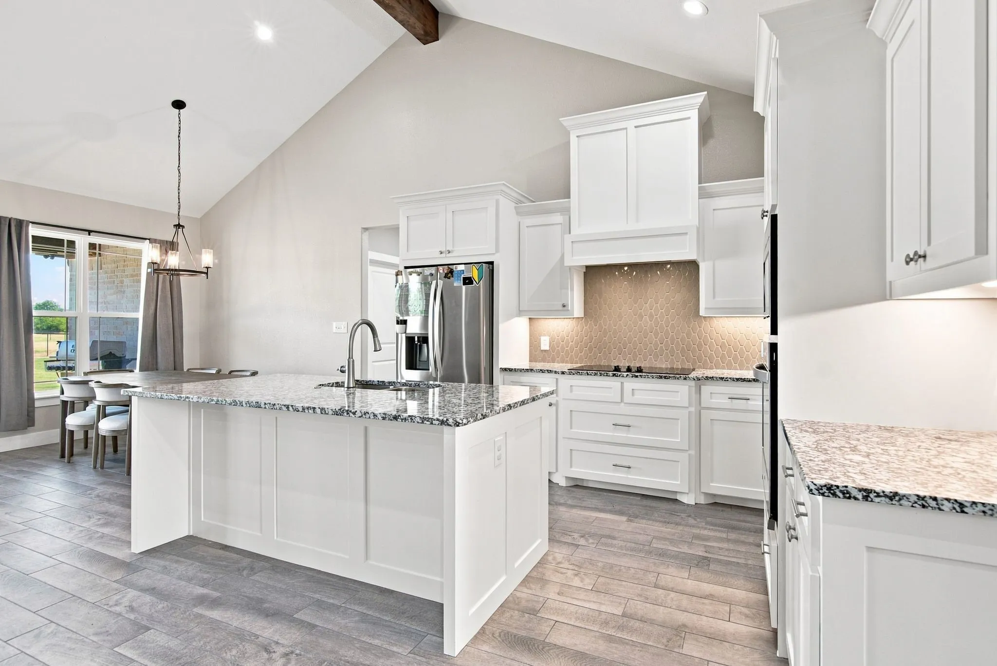 Kitchen featuring a central island with a stainless steel sink and faucet, white cabinetry, granite countertops, and wood-finish flooring