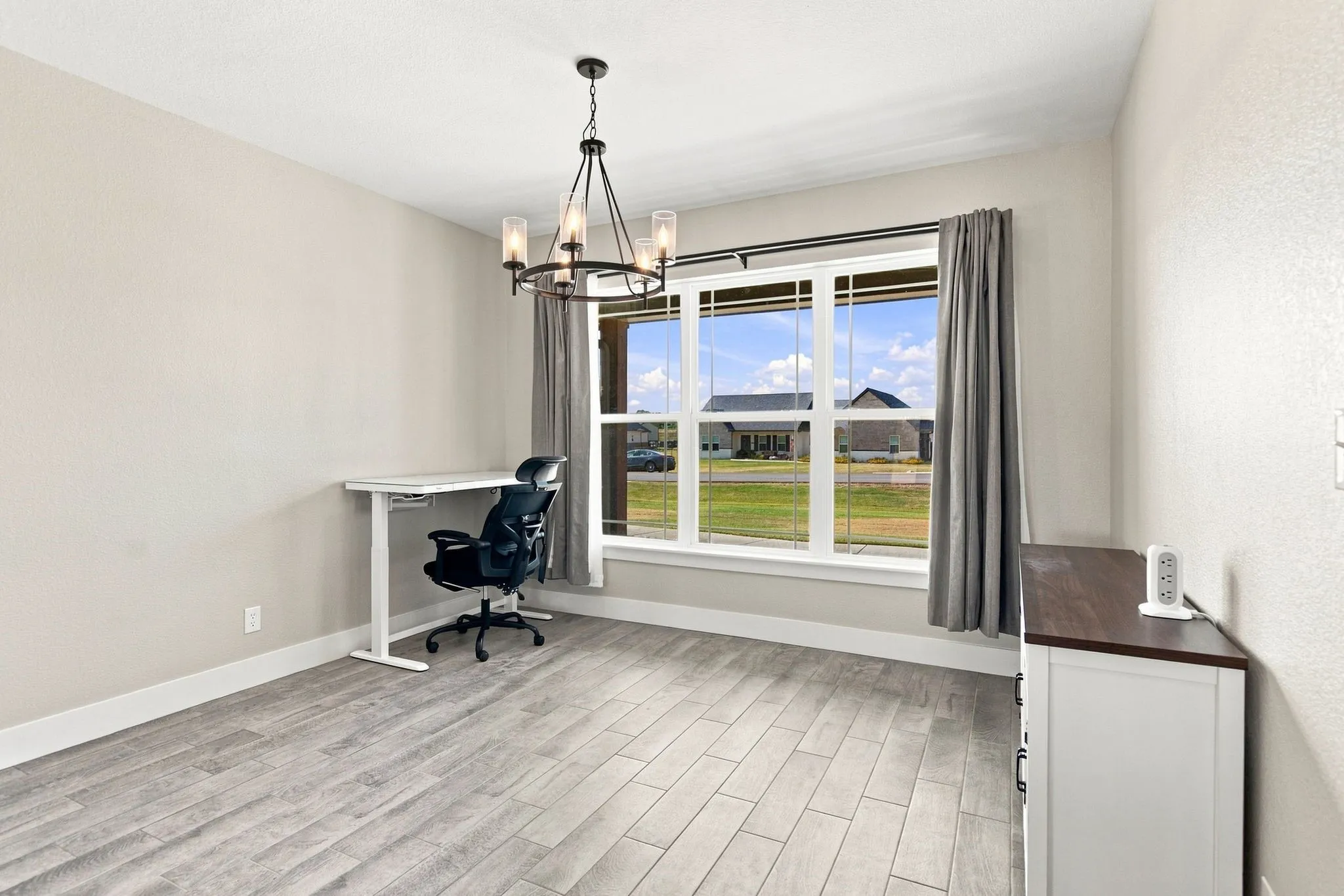 Spacious room featuring wood-finish flooring, a large multi-pane window, and a contemporary chandelier