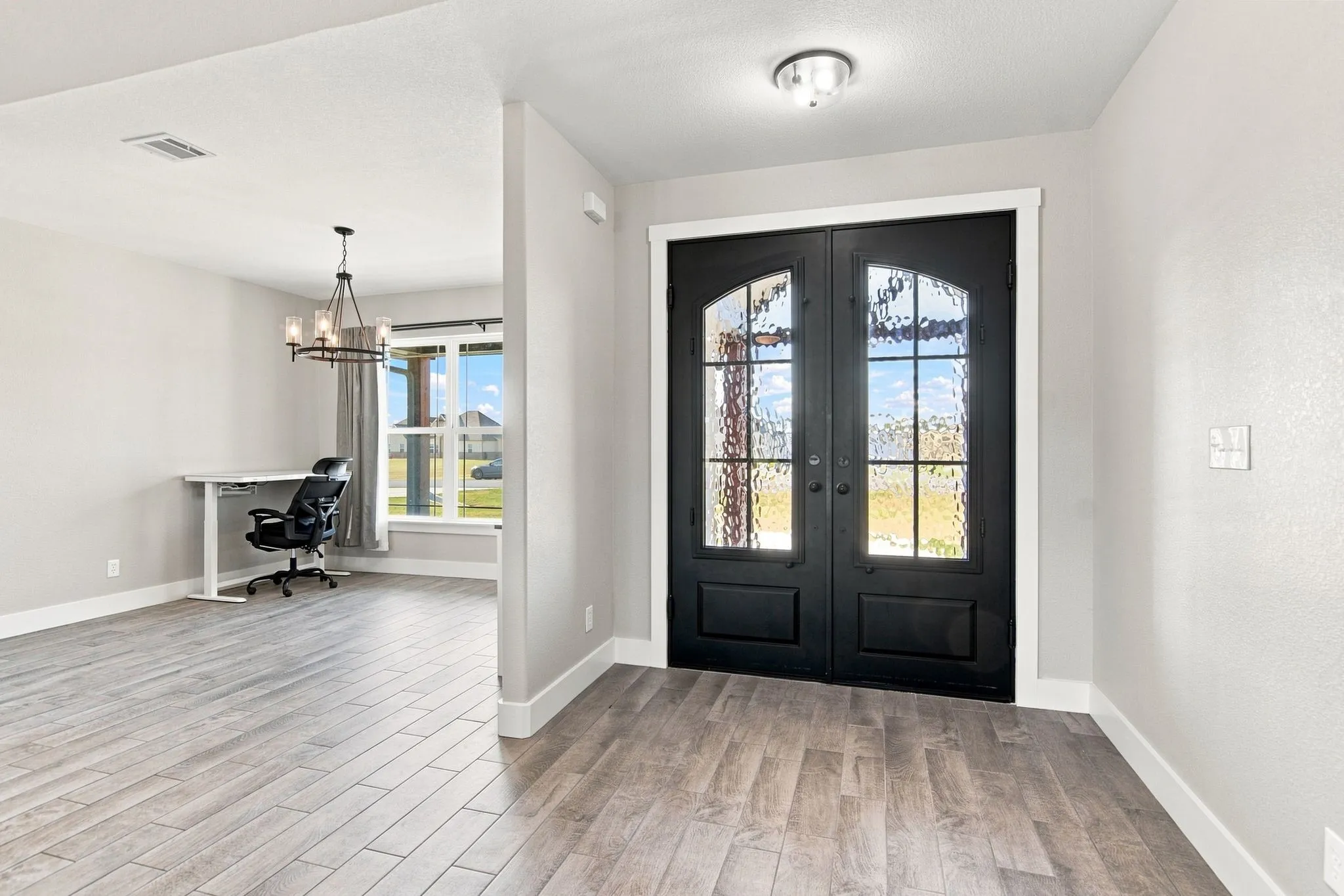 Welcoming foyer featuring elegant black double doors with decorative glass panes, light wood-finish plank flooring in a herringbone pattern, and clean white walls with substantial architectural trim