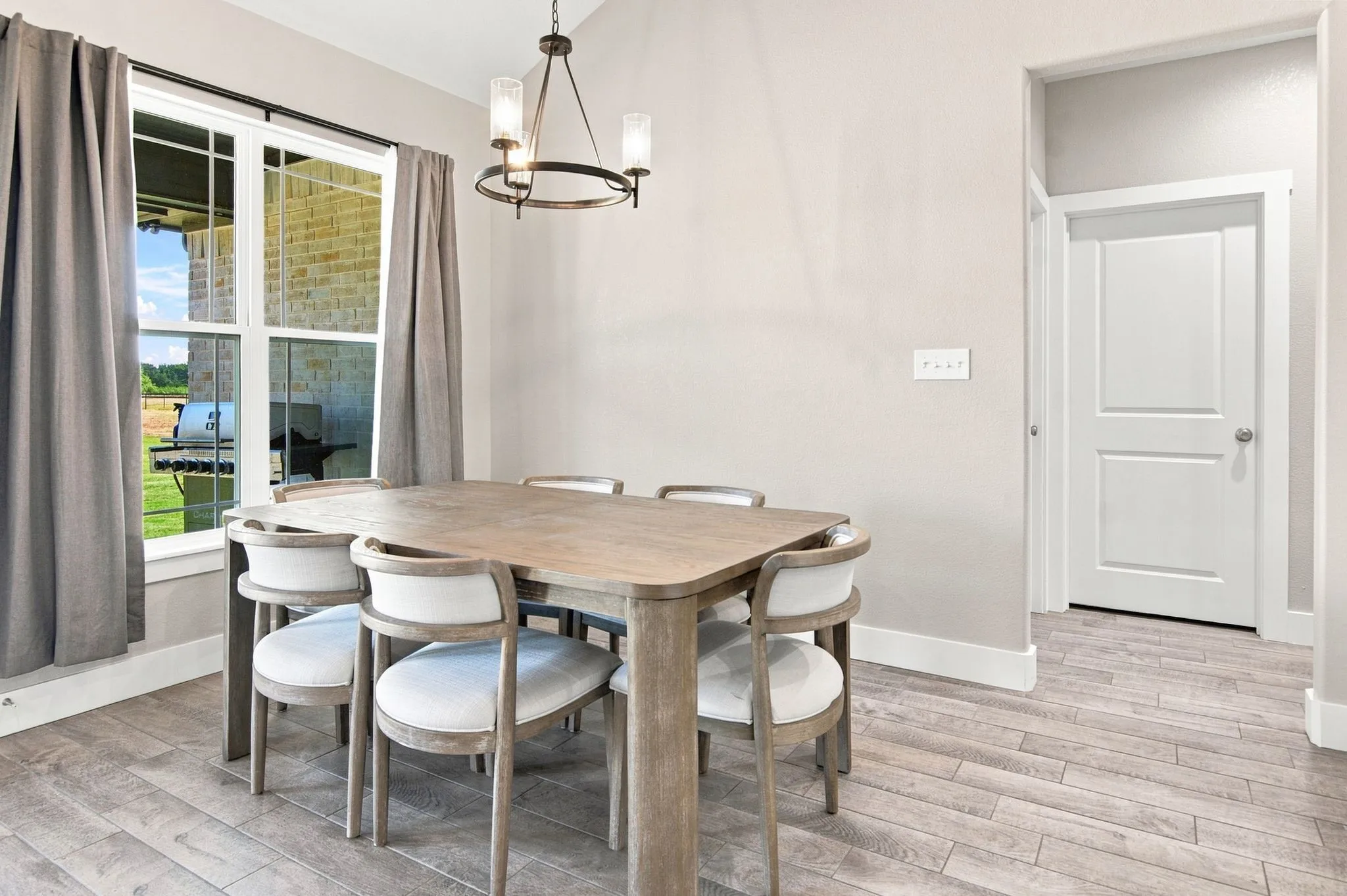 Dining area featuring wood-finish flooring, a contemporary chandelier, and a large window with white trim