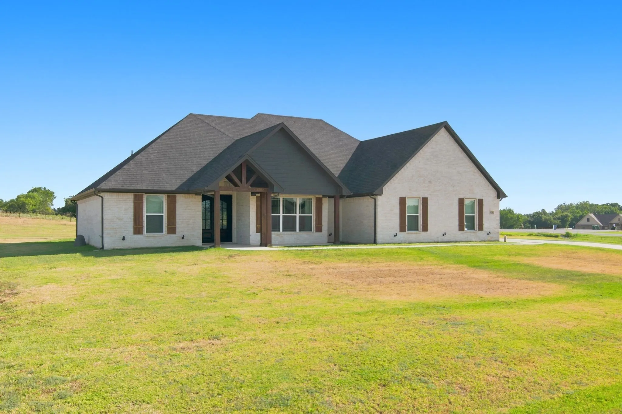Exterior showcasing light-colored brick, a dark shingle roof, and a prominent front entry with wood-beam detailing