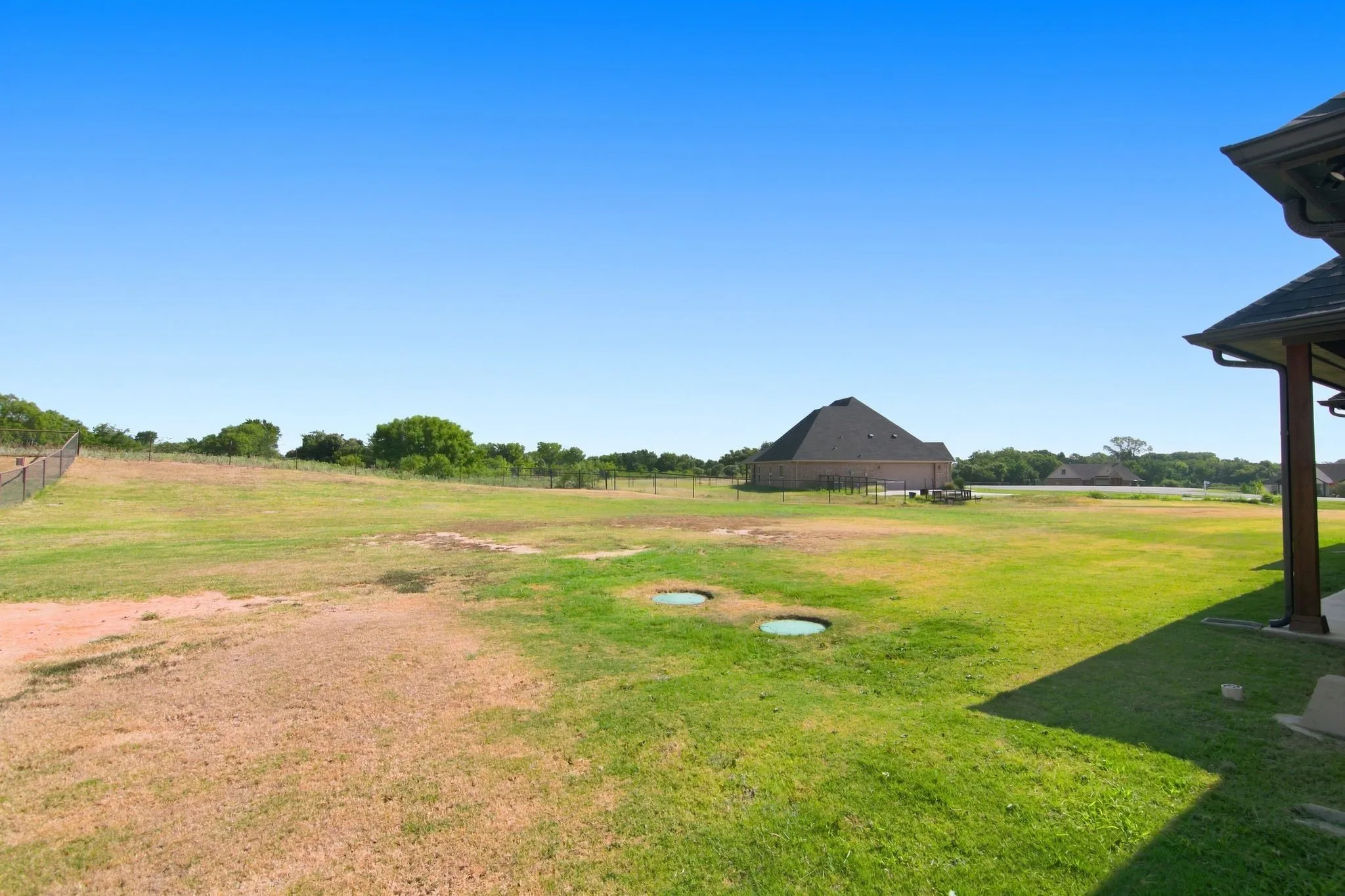Expansive outdoor space featuring a large lawn area and a partial view of a neighboring residence