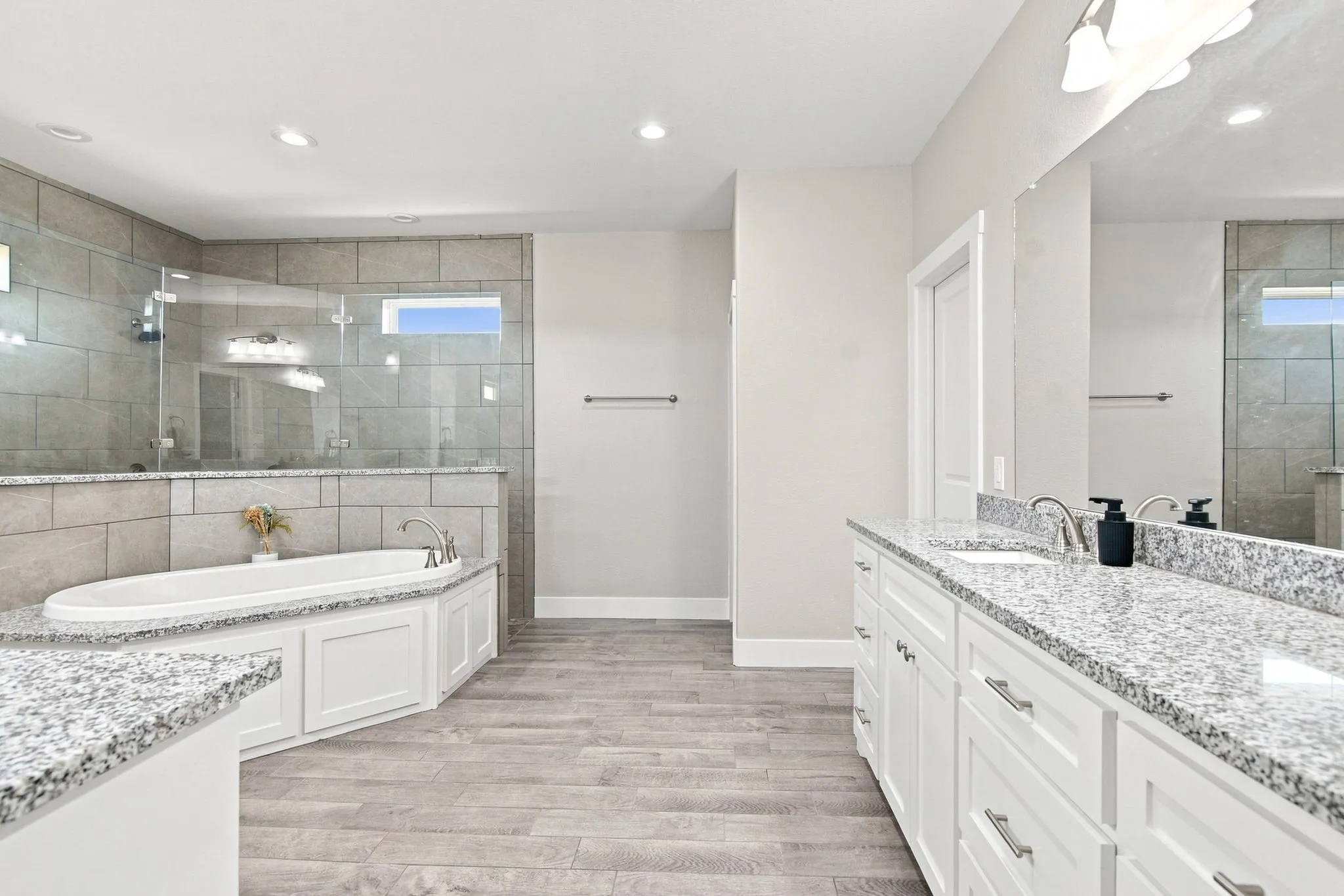 Spacious bathroom featuring a built-in soaking tub, a large glass-enclosed shower with tile surround, and a dual vanity with light-toned countertops