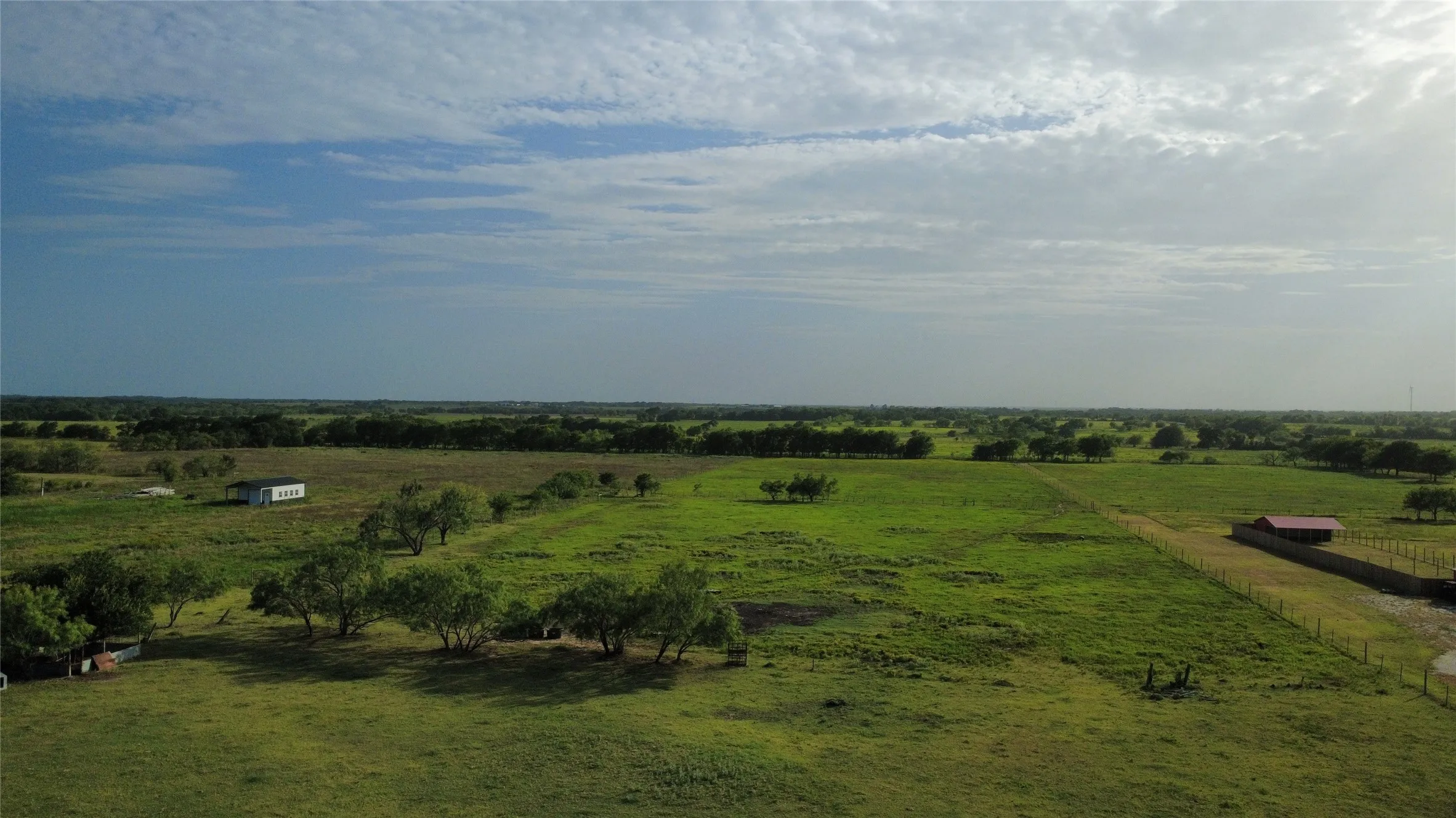 Expansive green acreage with scattered mature trees and a distant white structure